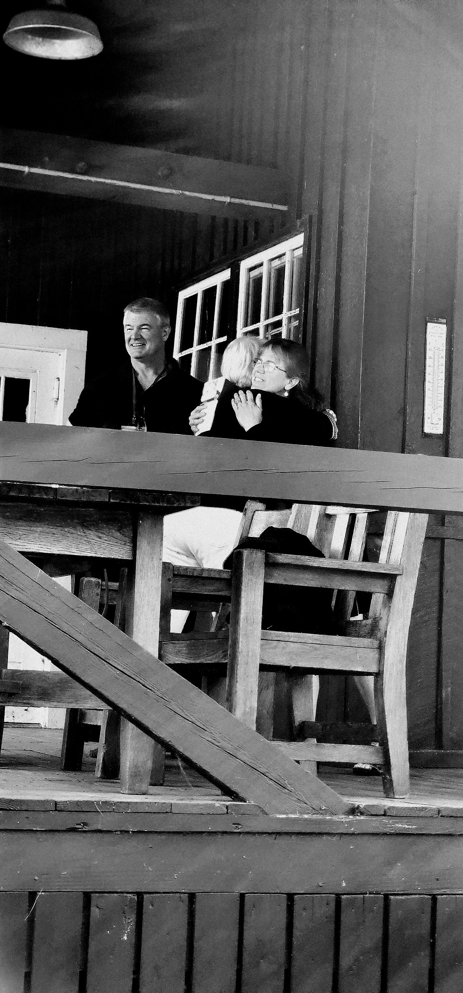 Two people hugging on a porch with a third person in the background