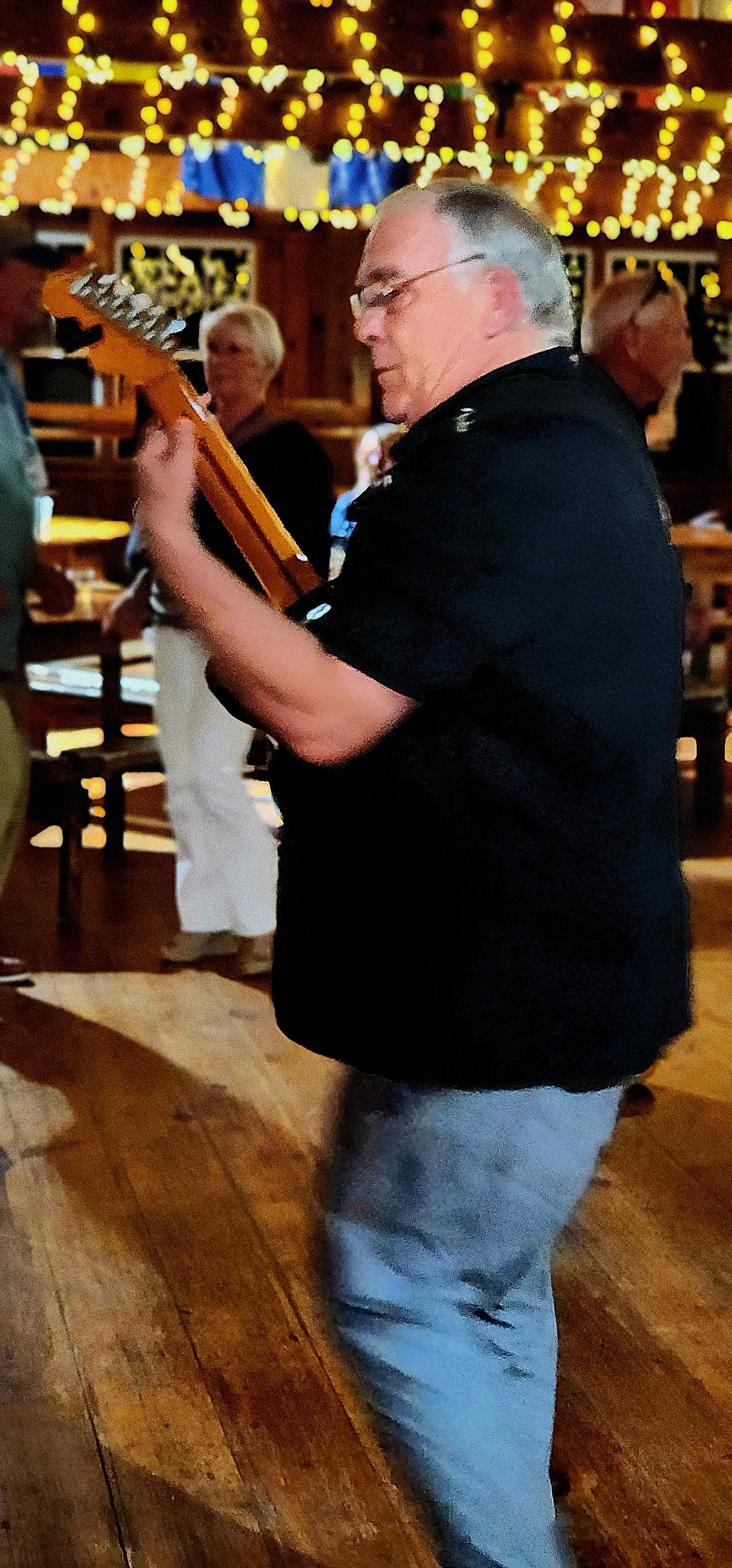 A man, wearing a black shirt and jeans, playing guitar