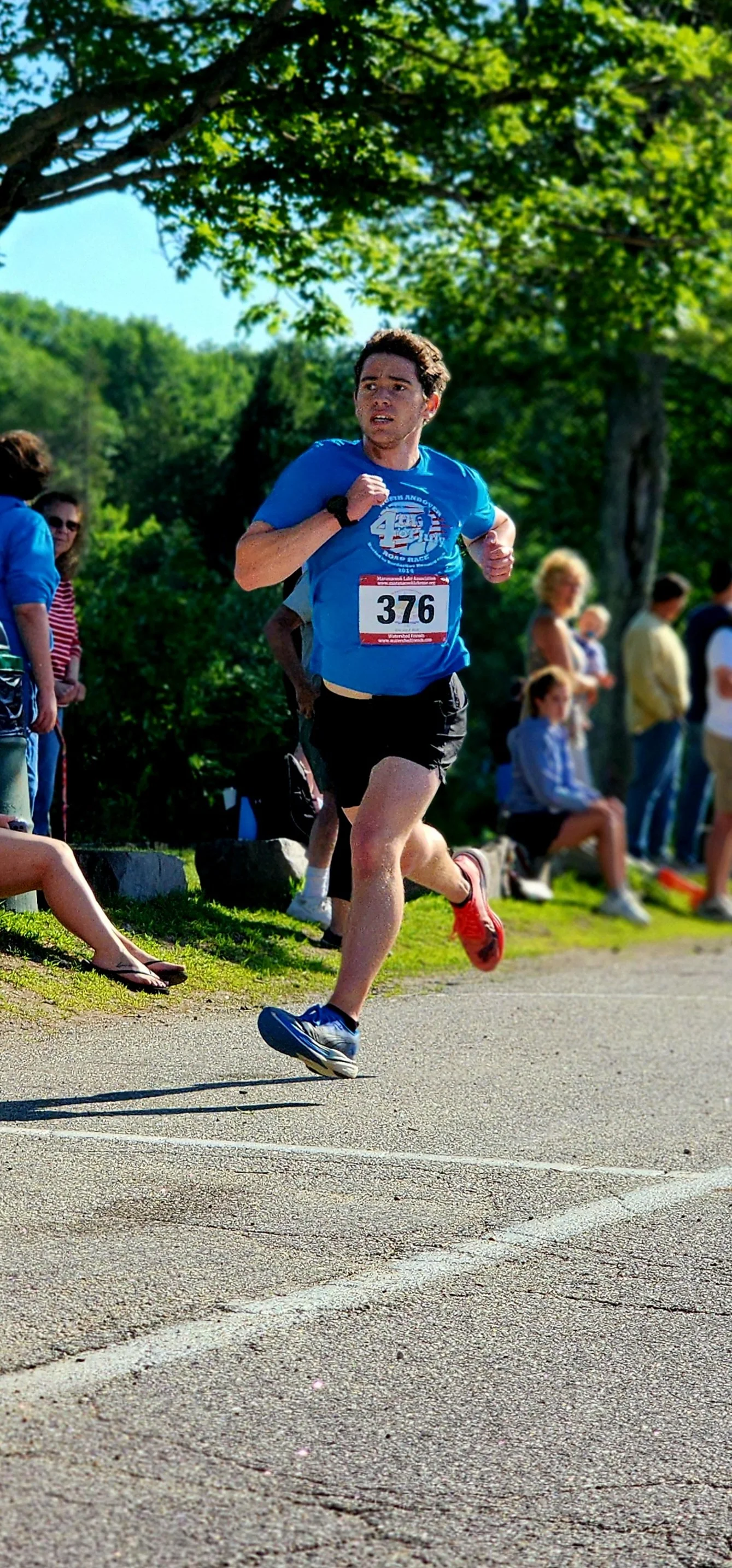A man wearing a blue t-shirt and black shorts running with a crowd standing behind him