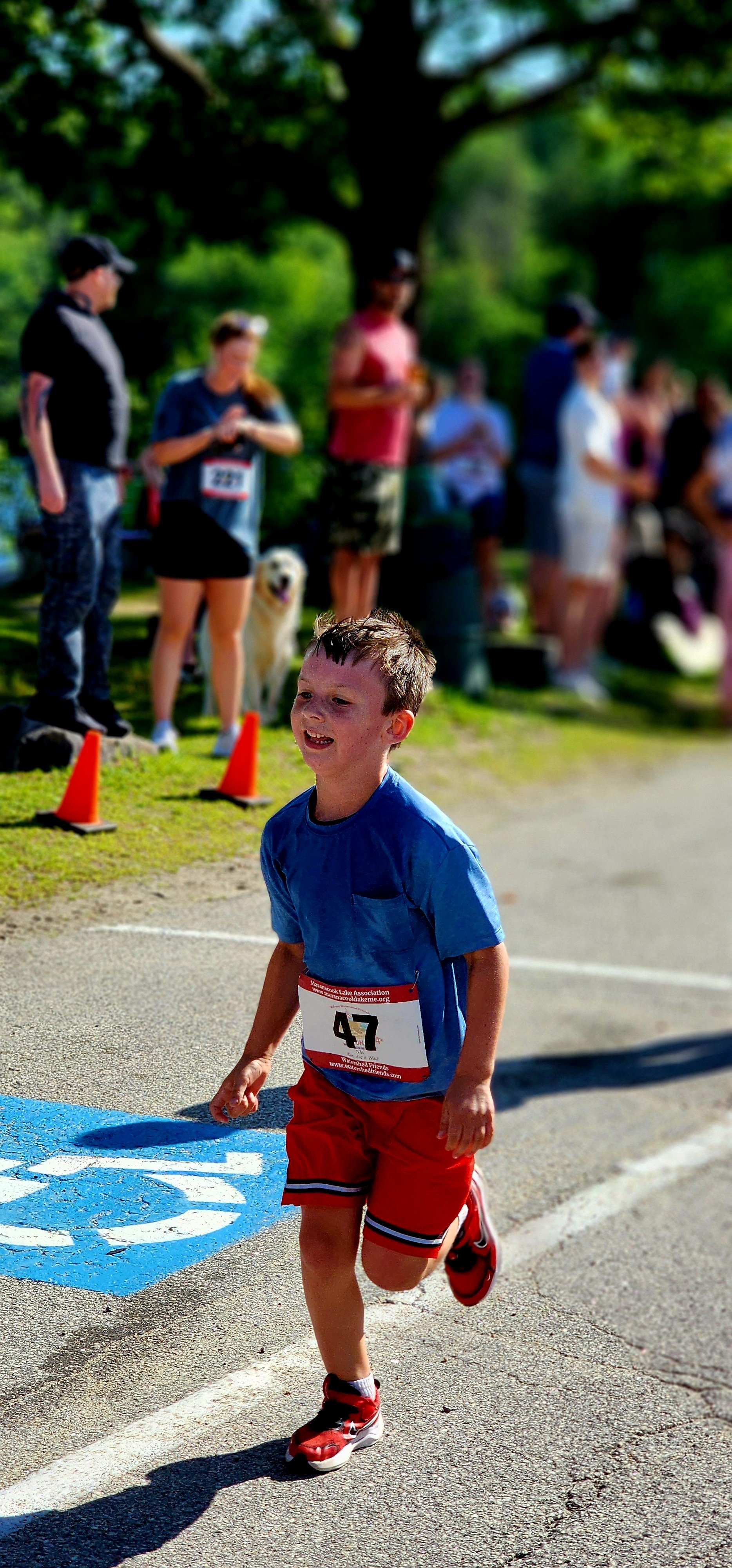 A young boy wearing a blue t-shirt and red shorts running with a crowd standing in the background