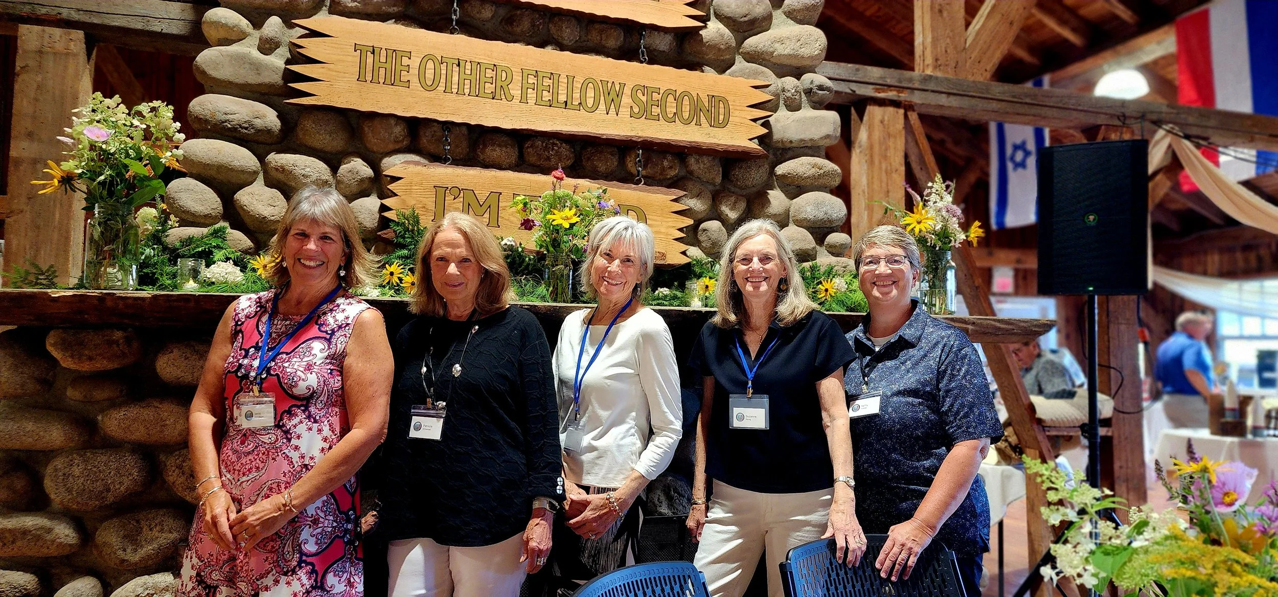 Five women standing in front of a fireplace mantle that is covered in greenery