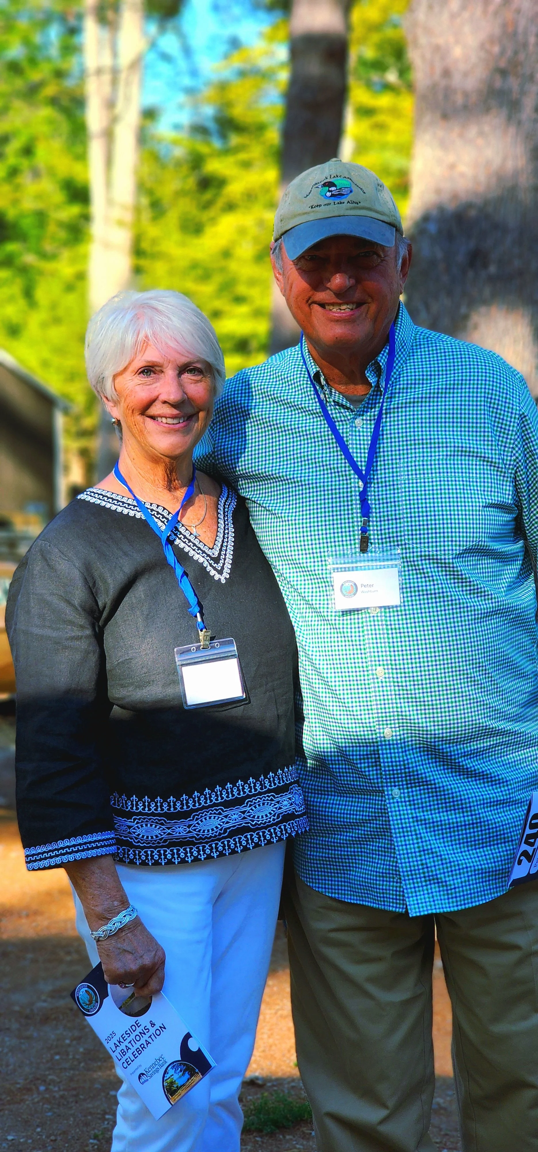 A woman, wearing a black long sleeve shirt and white pants, and a man, wearing a blue long sleeve shirt and khaki pants, smiling at the camera