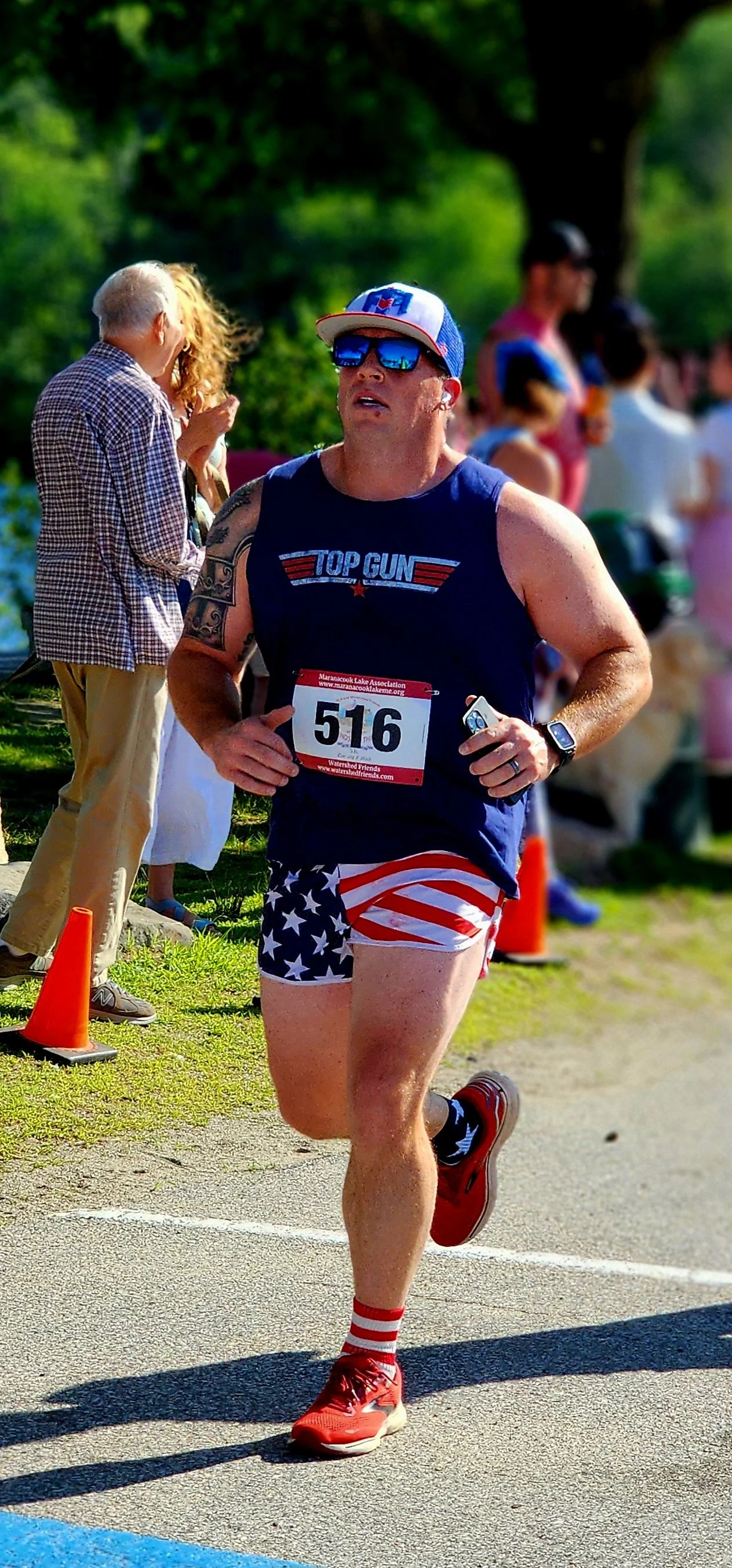 A man wearing a navy tank top and American flag printed shorts running with a crowd standing in the background