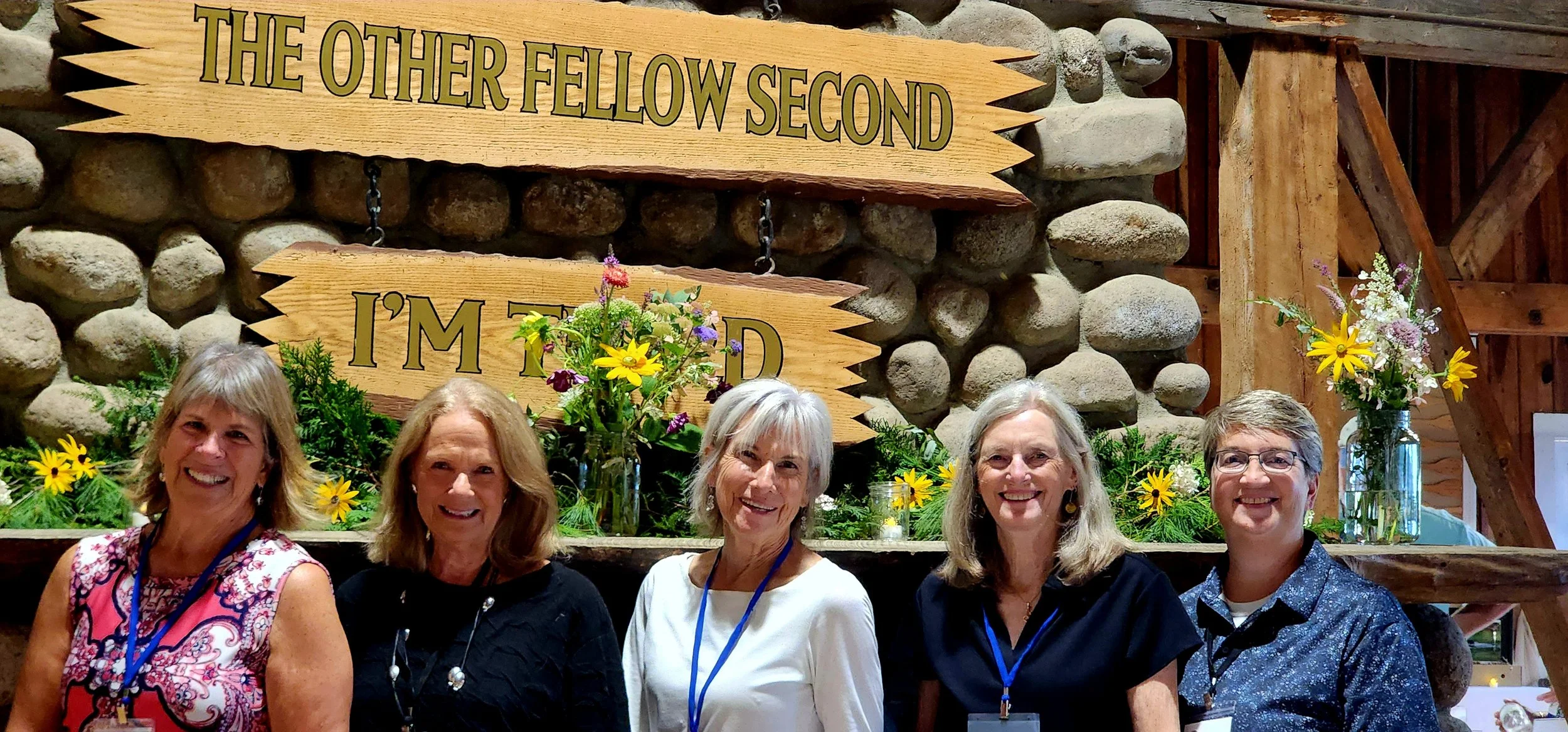 Five women standing in front of a fireplace mantle that is covered in greenery