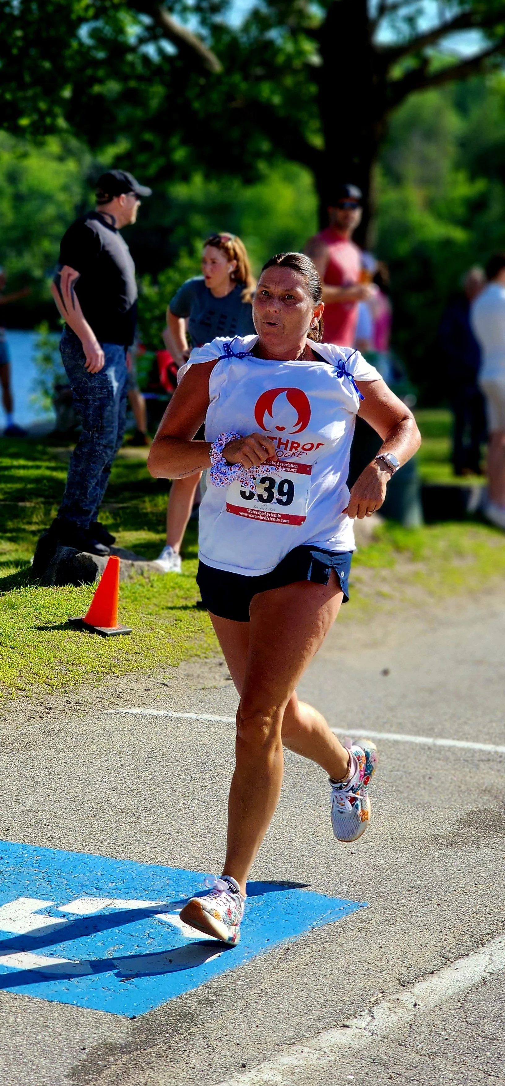 A woman wearing a white t-shirt and black shorts running with a crowd standing in the background