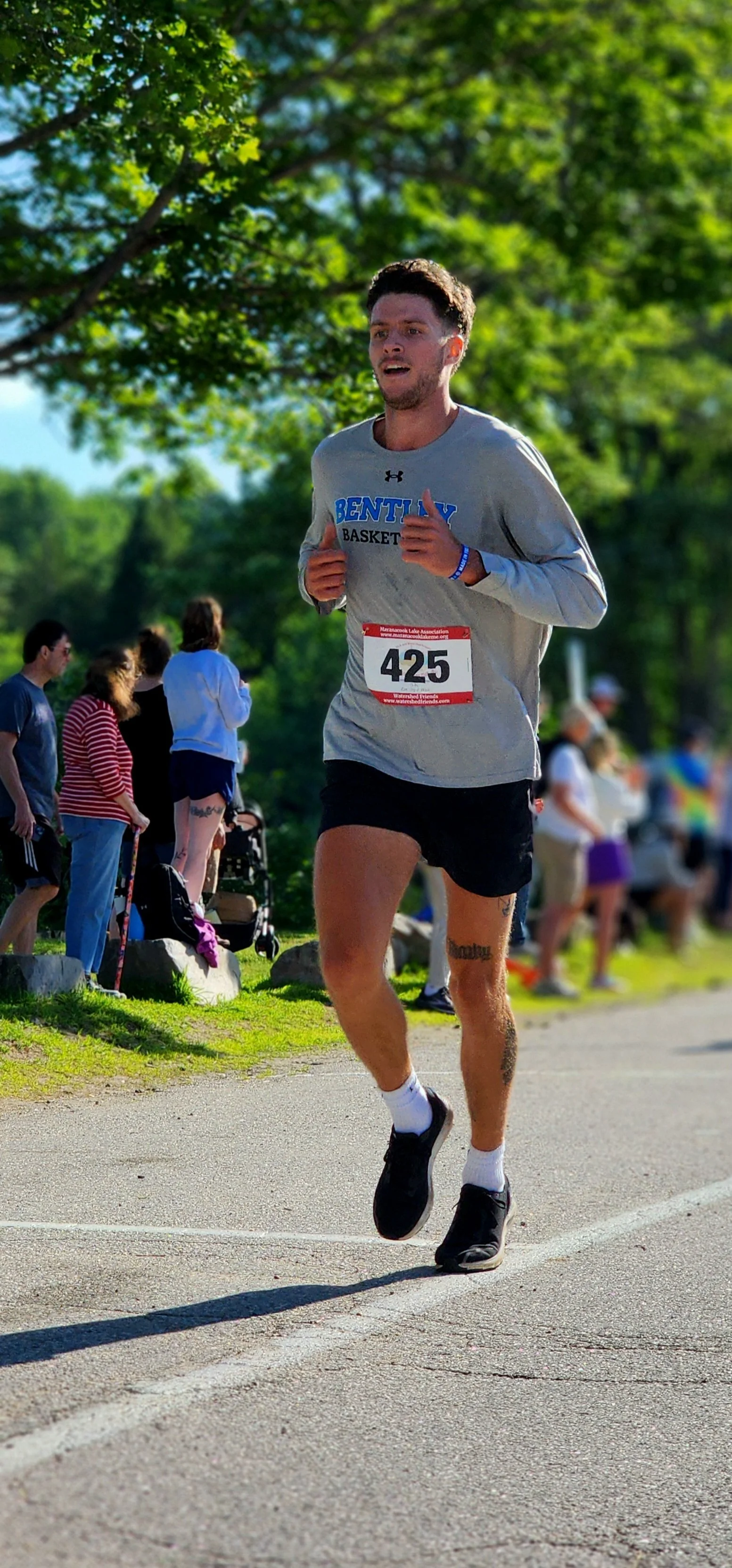 A man wearing a grey long sleeve shirt with black shorts running with a crowd standing behind him