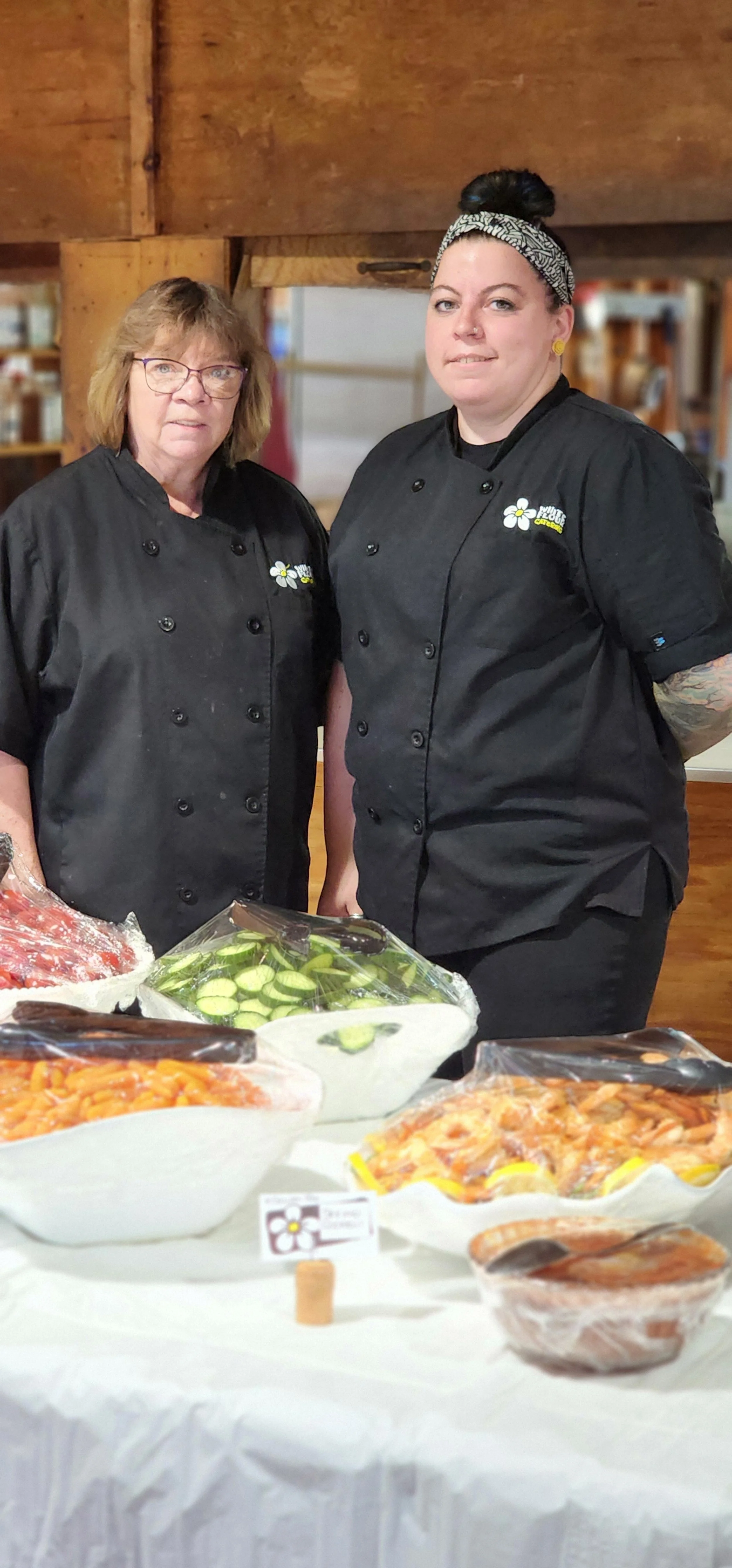 Two women dressed in black server uniforms standing behind a buffet table