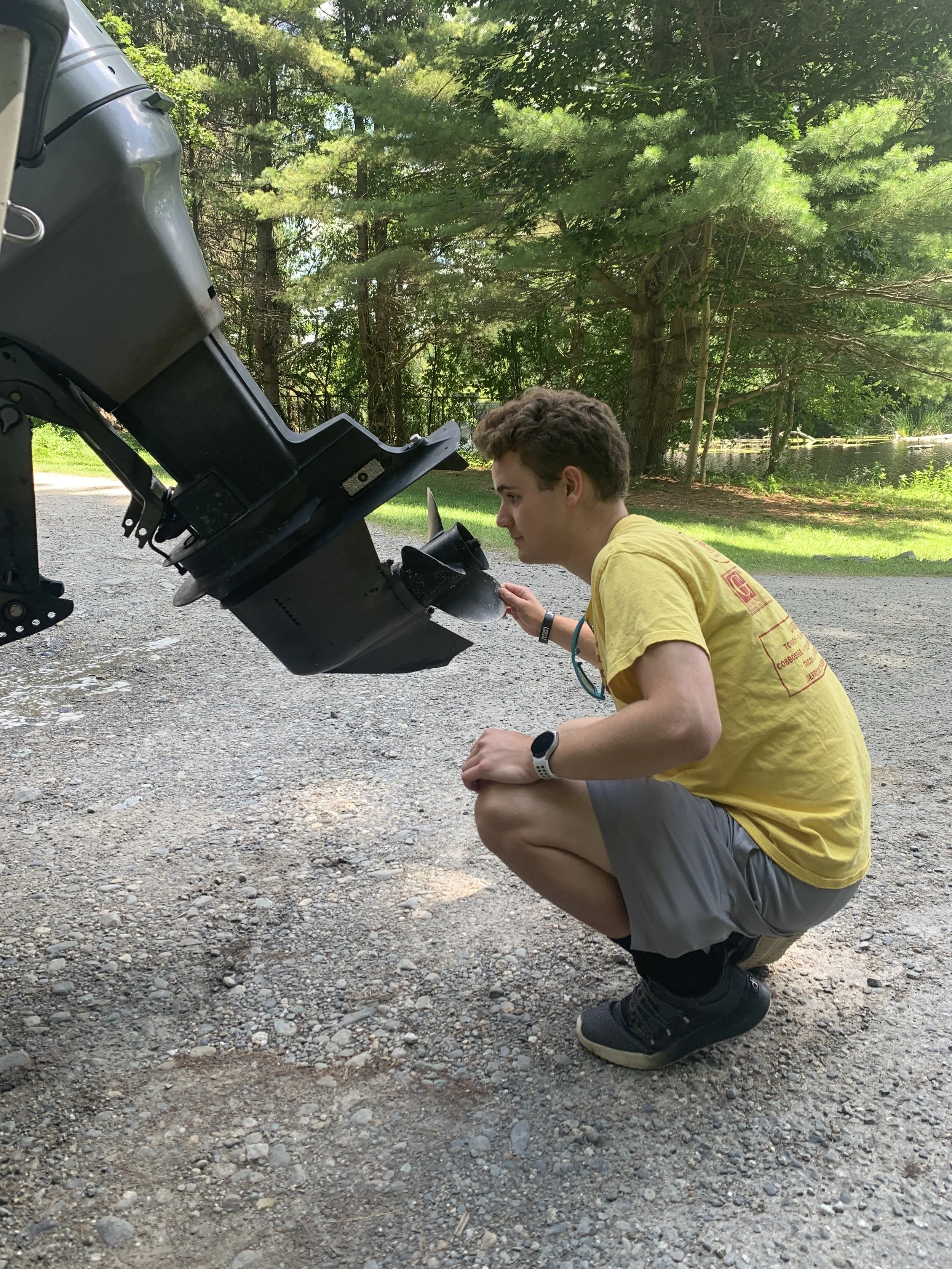 A boy, wearing a yellow t-shirt, examining the prop of a boat that is on a trailer