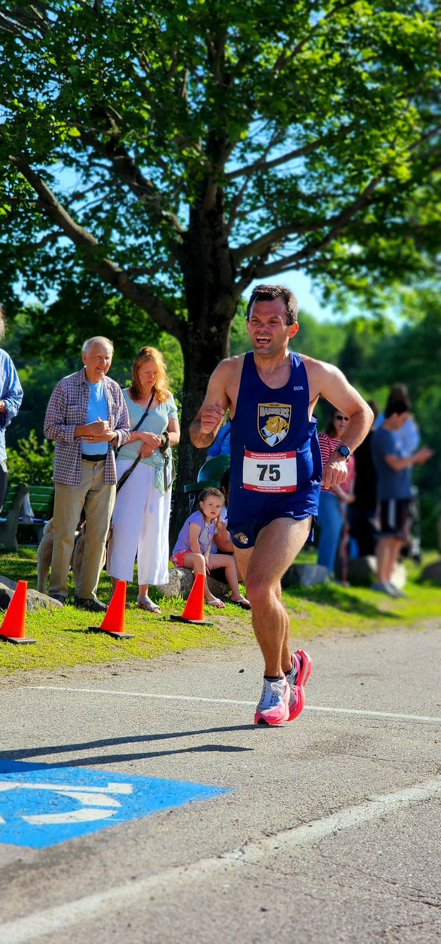 A man wearing a blue tank top and shorts running with a crowd standing behind him
