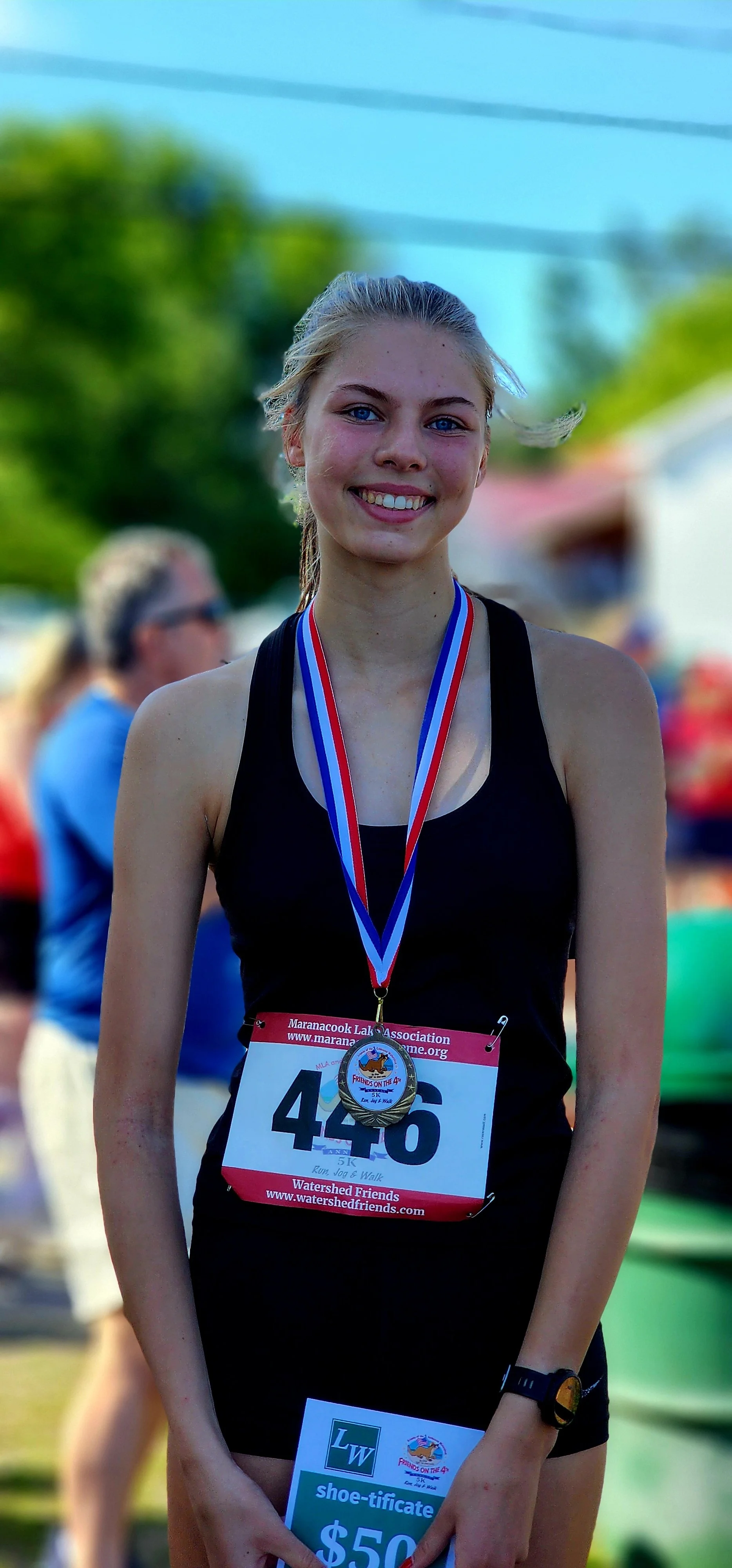 A girl smiling at the camera, wearing a prize medal, black tank top, and black shorts