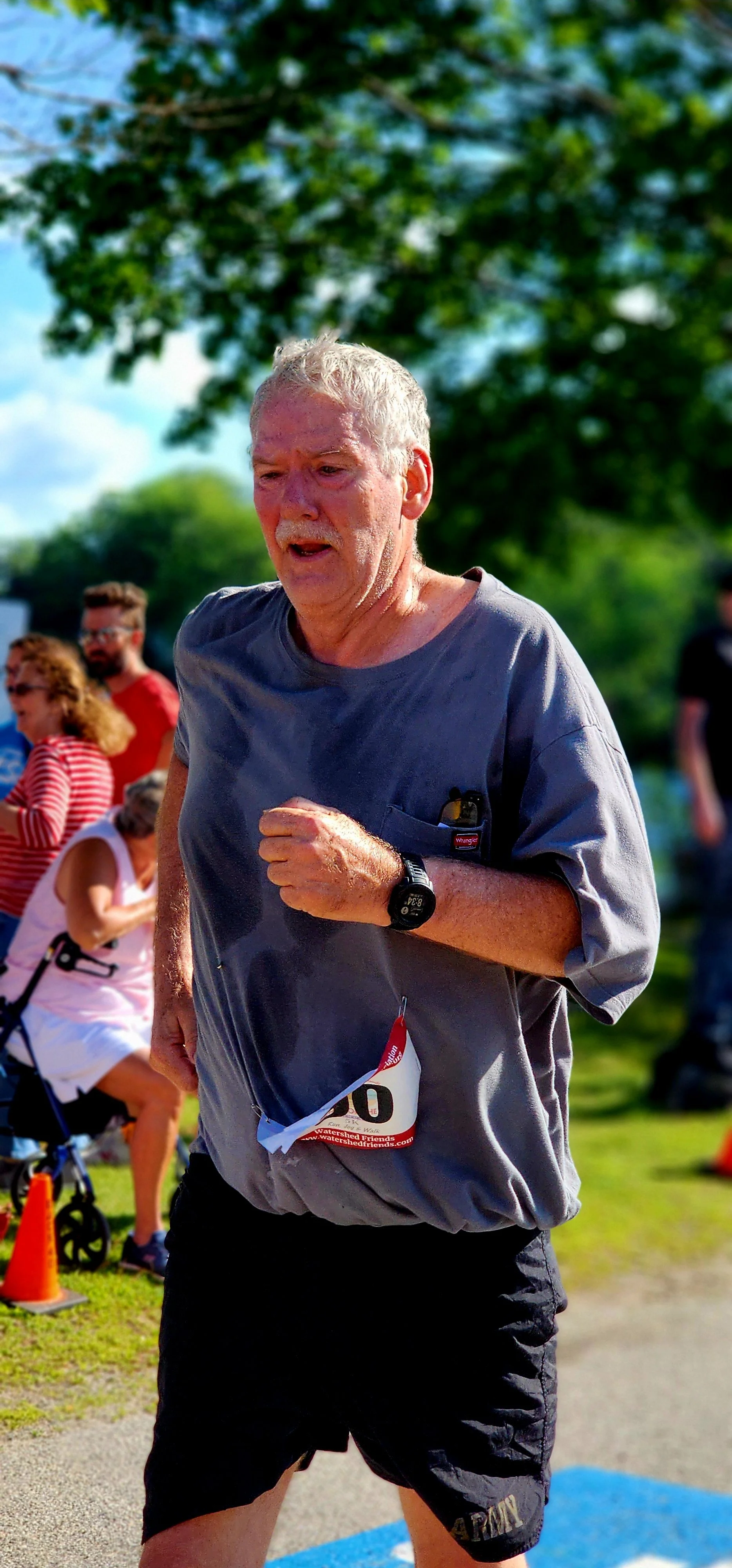 A man wearing a grey t-shirt and black shorts running with a crowd standing in the background