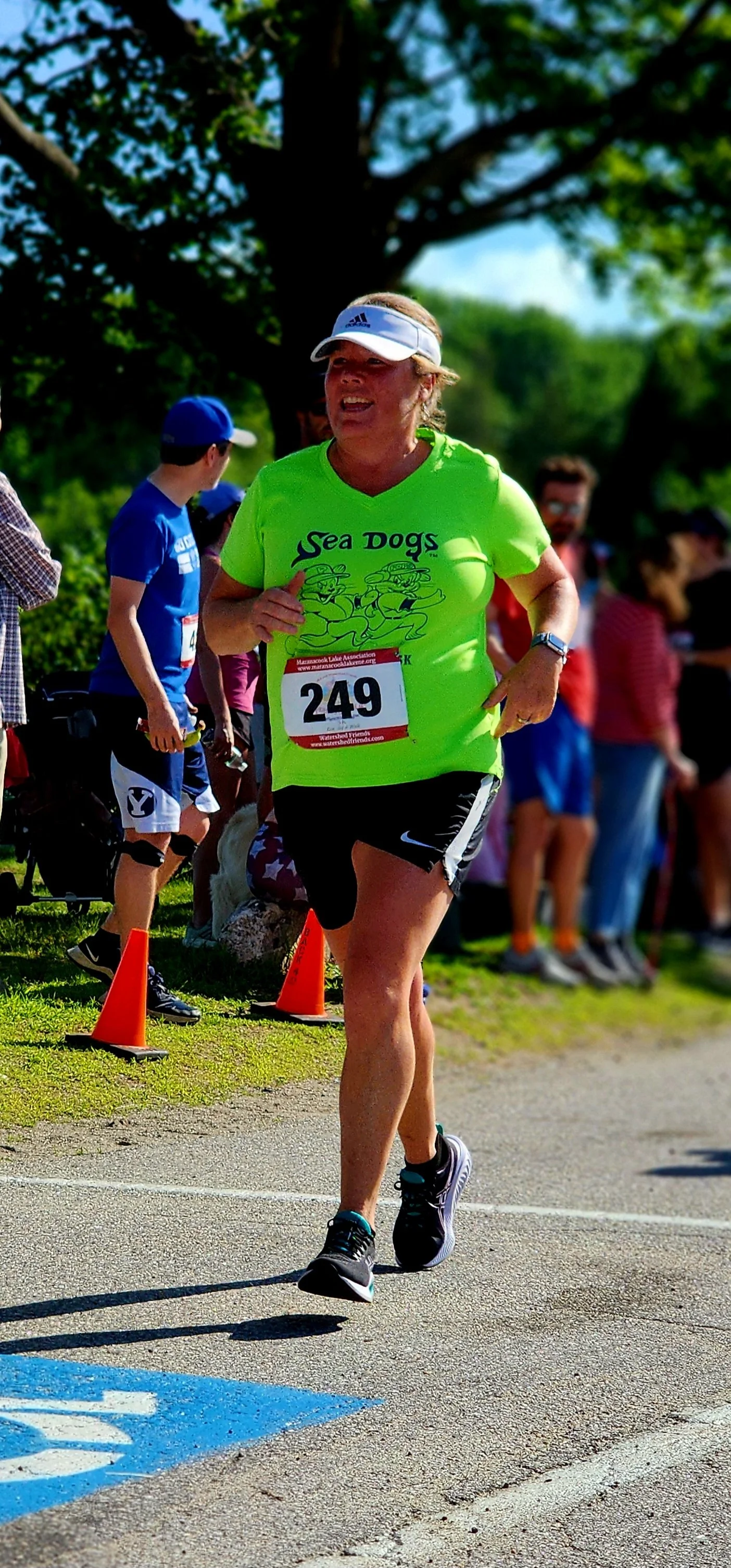 A woman wearing a neon green t-shirt and black shorts running with a crowd standing the background