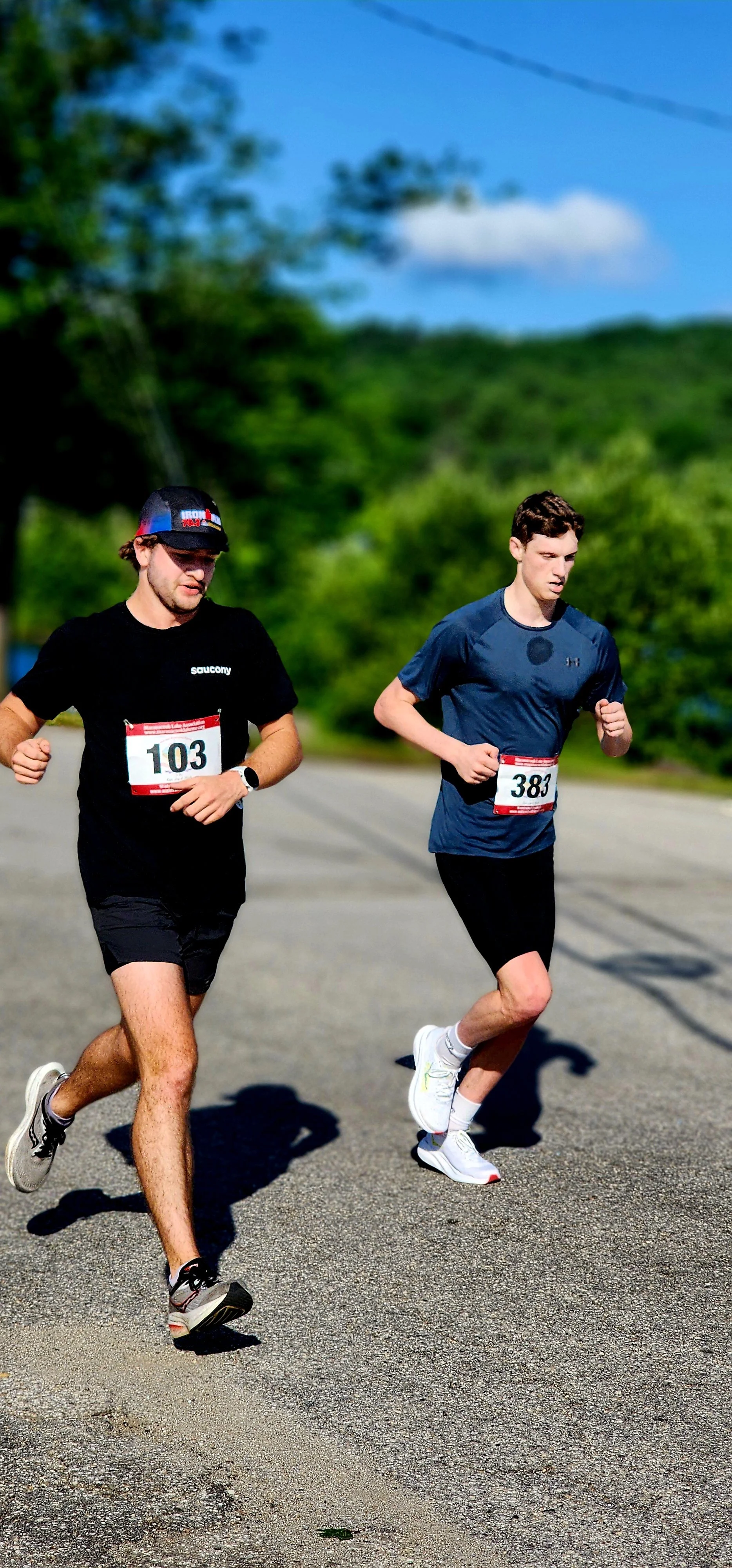 Two men running, the one of the left in a black t-shirt and shorts, the one on the right wearing a navy t-shirt and black shorts 