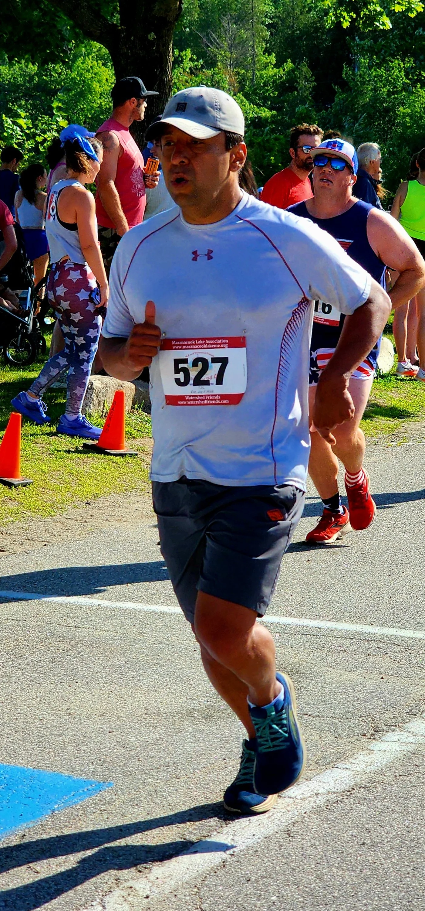 A man wearing a white t-shirt and grey shorts running with a crowd standing in the background