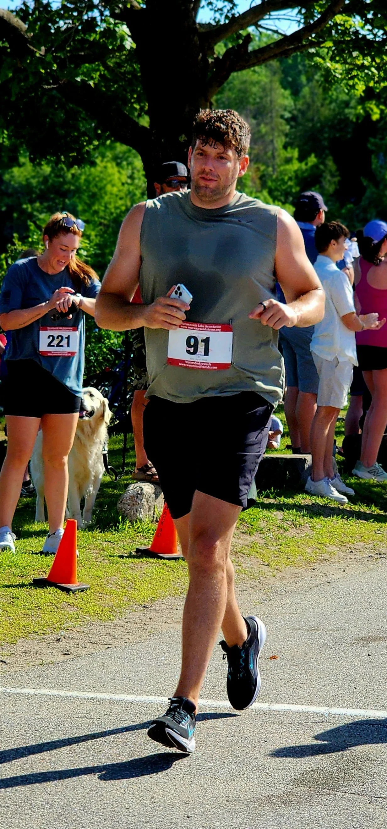 A man wearing a grey t-shirt and black shorts running with a crowd standing in the background