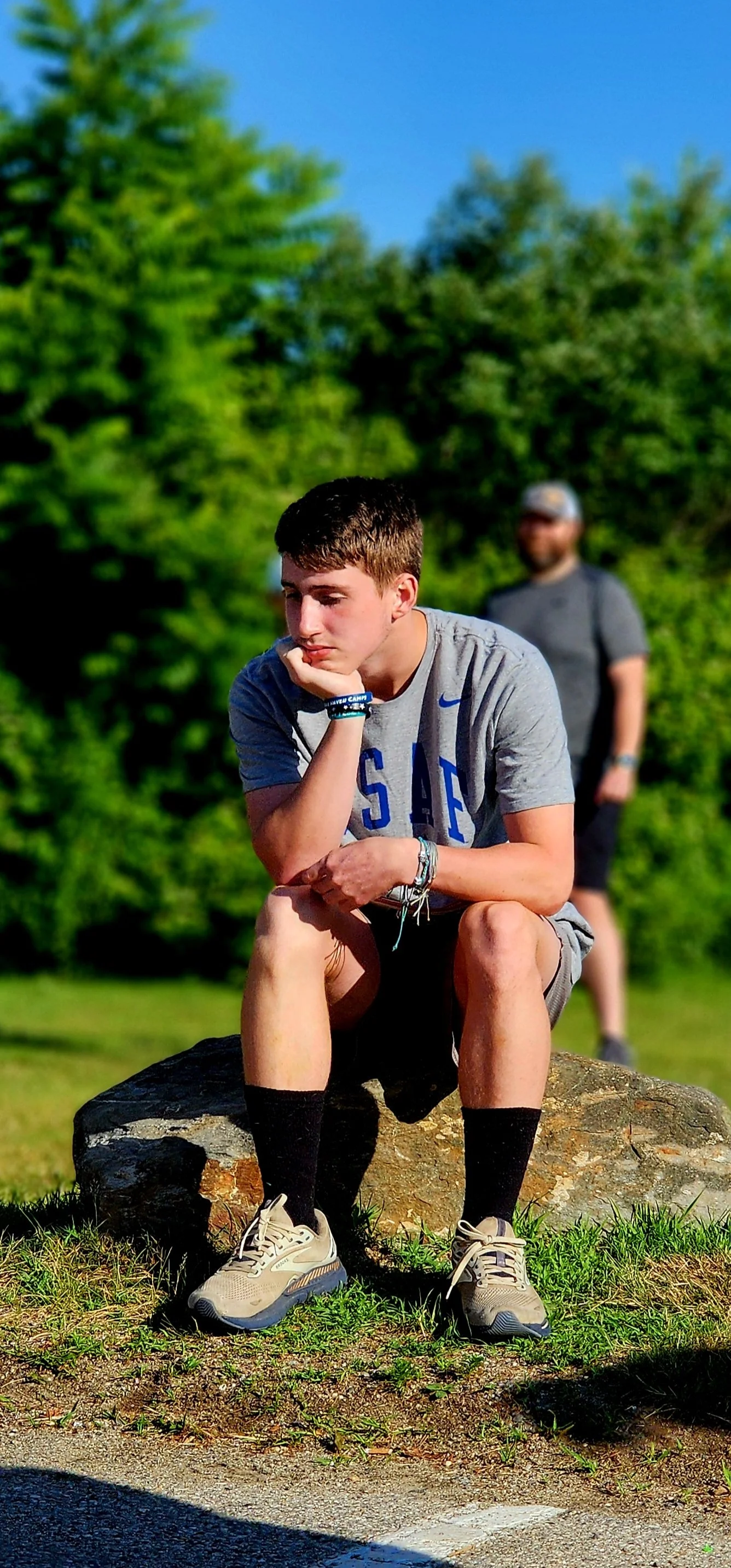 A man, wearing a grey t-shirt, sitting on a rock