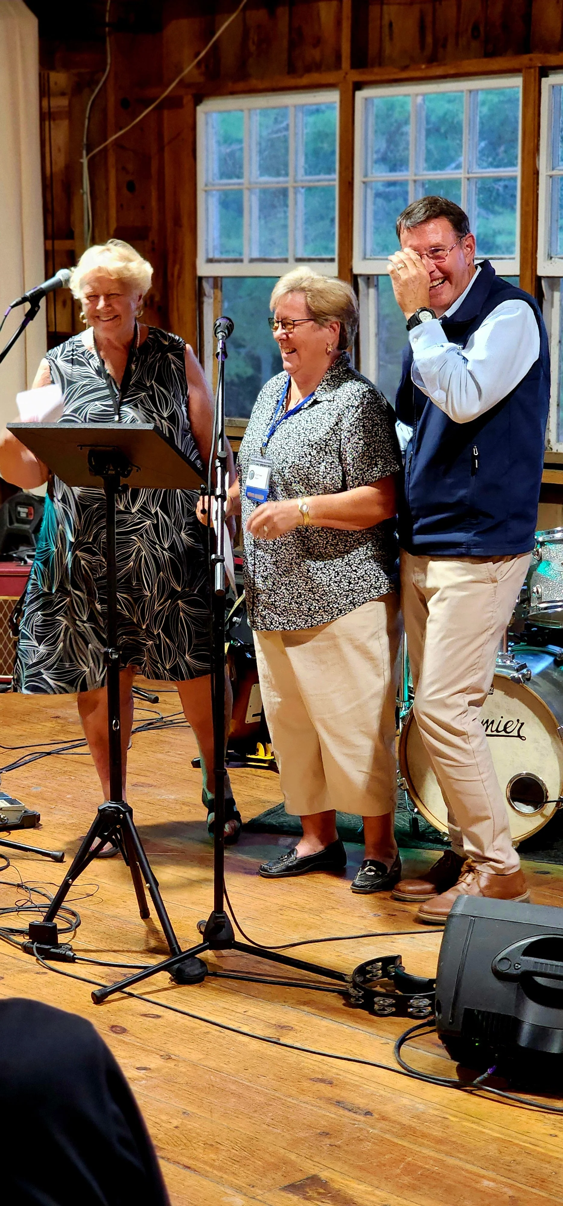 Two women and a man, the woman on the left has a stand and microphone in front of her