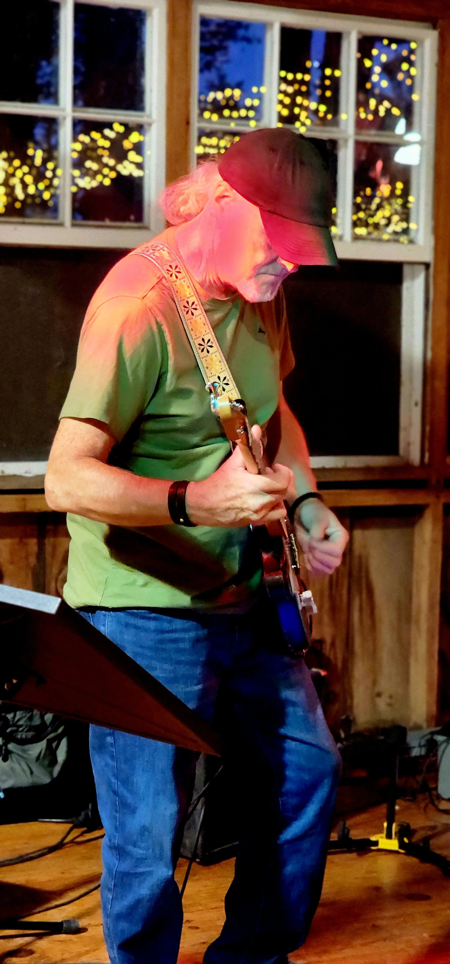 A man, wearing a green t-shirt and jeans, playing guitar