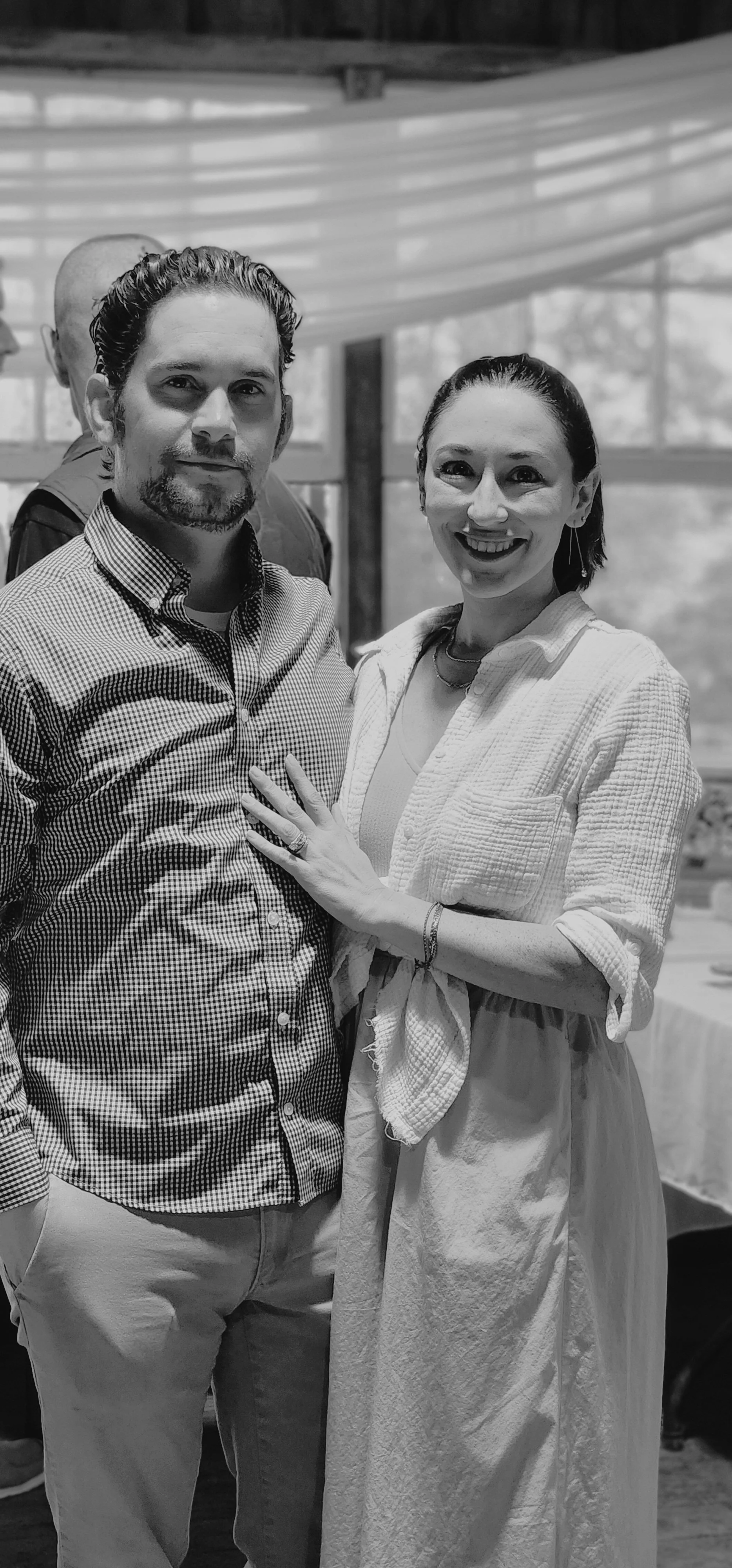 A man, wearing a button up shirt, and a woman wearing a long dress, smiling at the camera