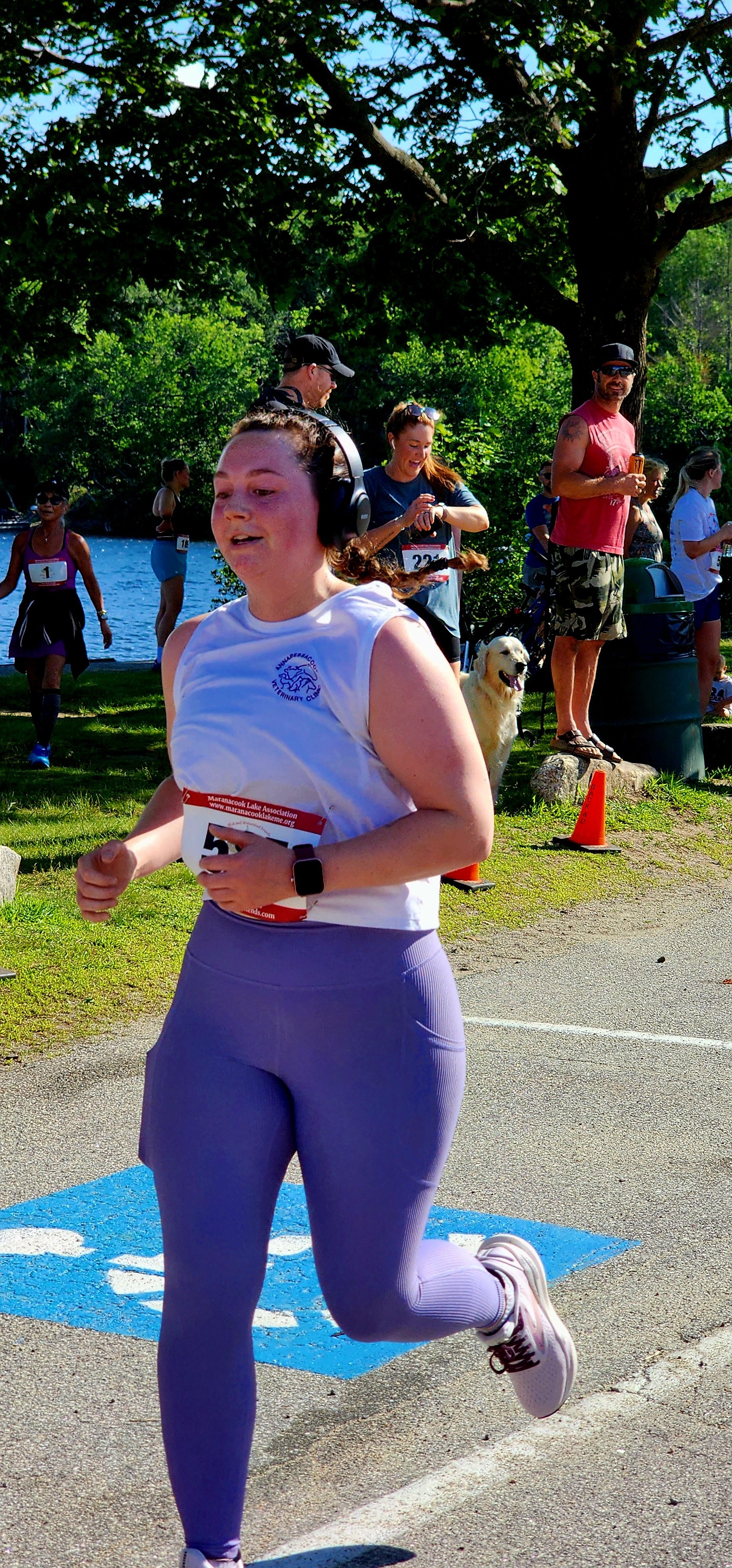 A woman wearing a white tank top and purple leggings running with a crowd standing in the background
