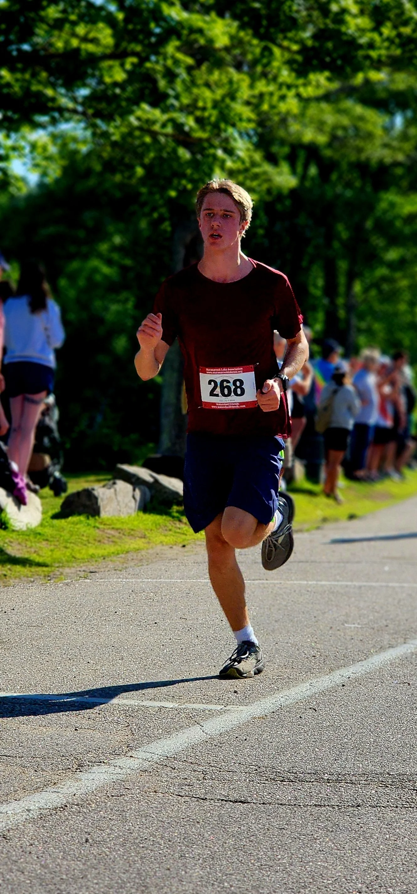 A man wearing a black t-shirt and shorts running with a crowd standing in the background