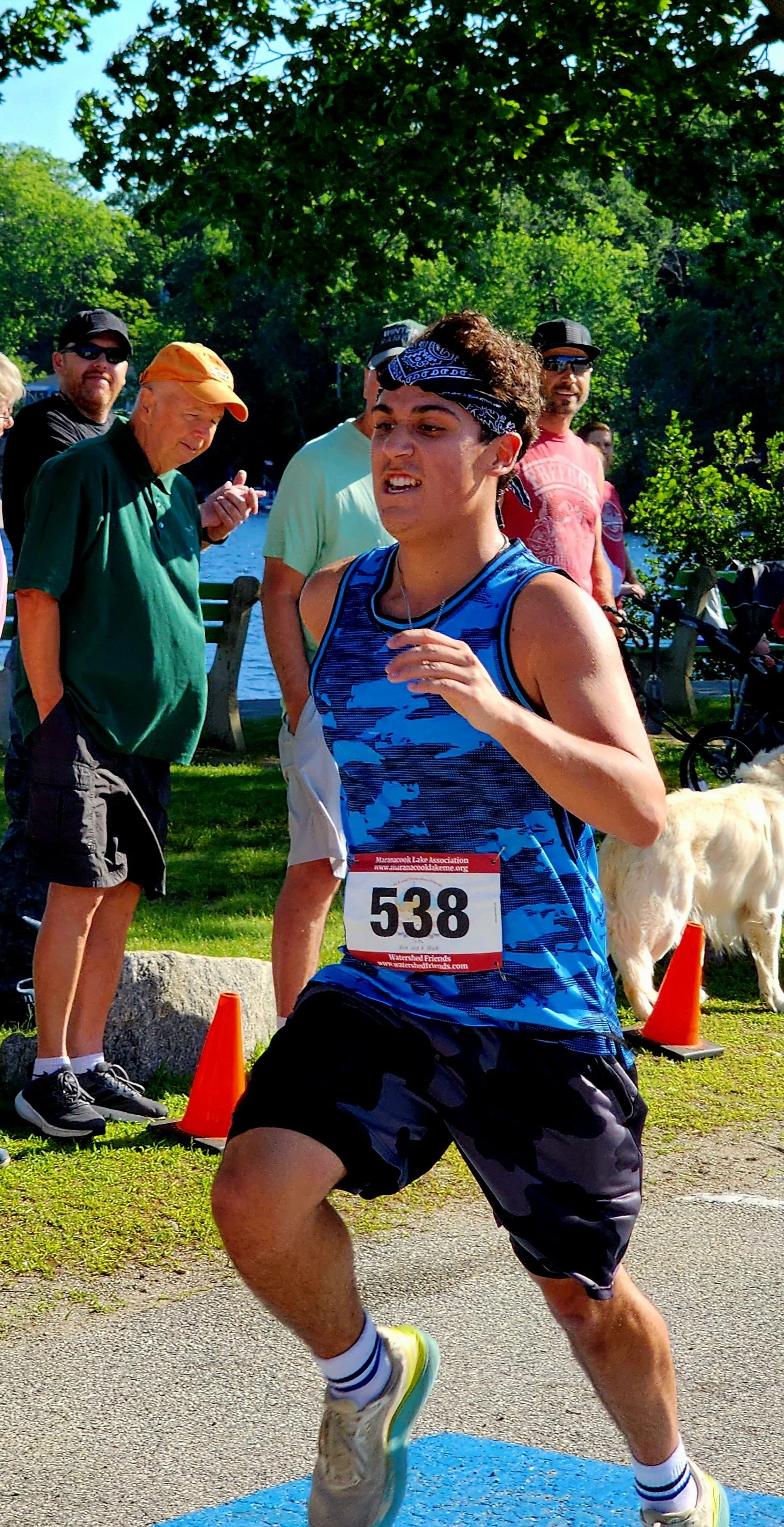 A person wearing a blue camo patterned tank top and black short running with a crowd standing in the background