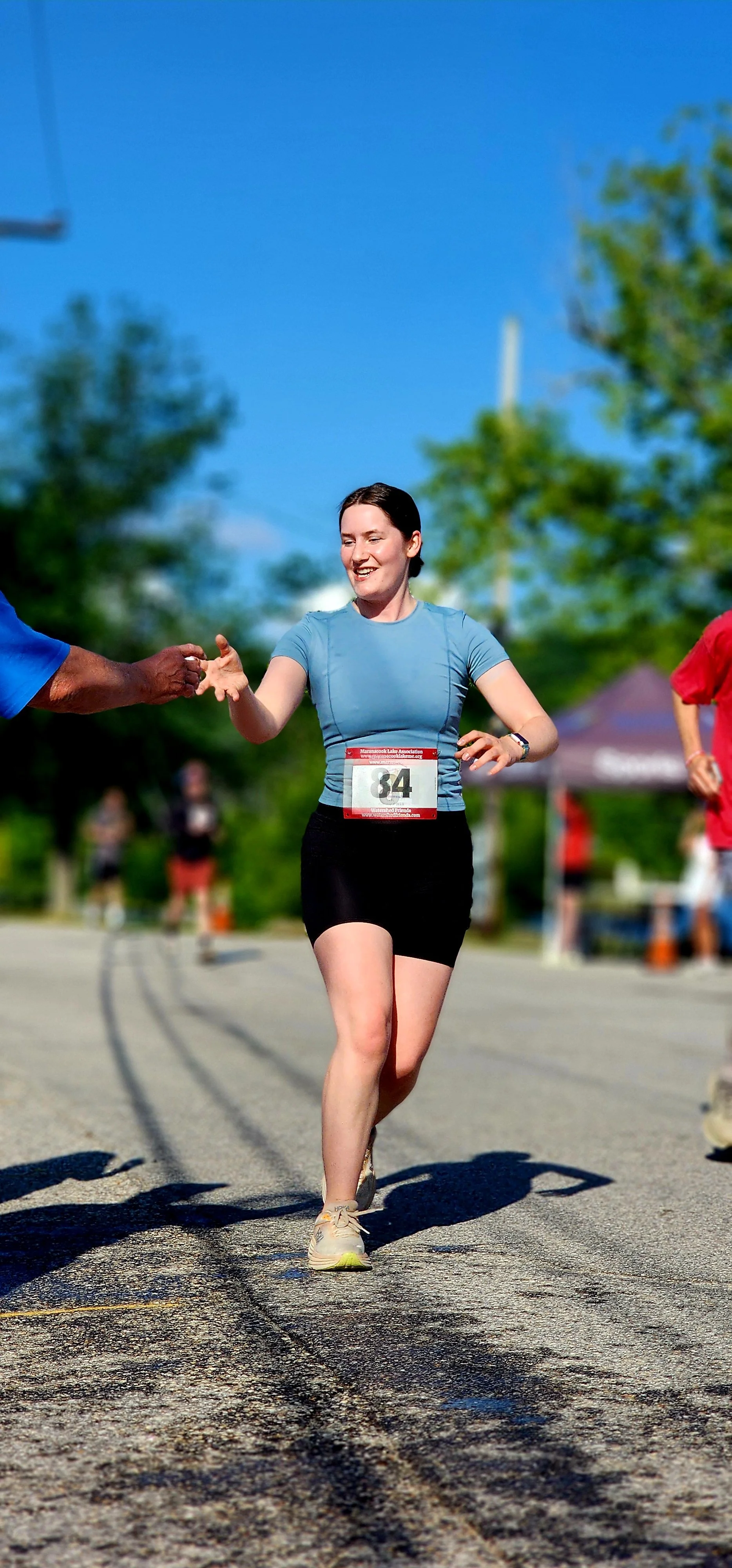 A woman wearing a teal t-shirt and black shorts being handed a cup of water as she runs
