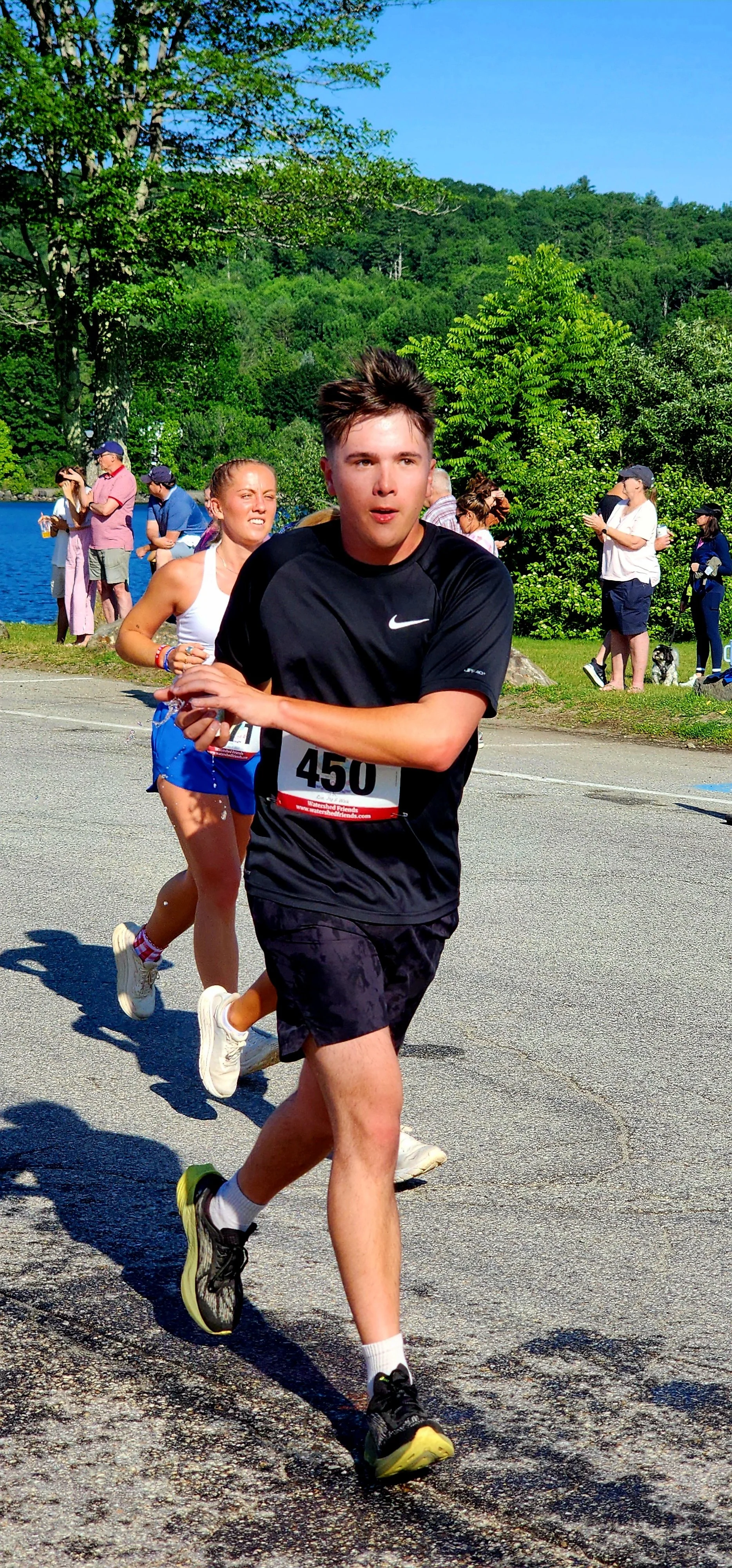 A man wearing a black t-shirt and shirts clutching a cup of water in both hands as he runs