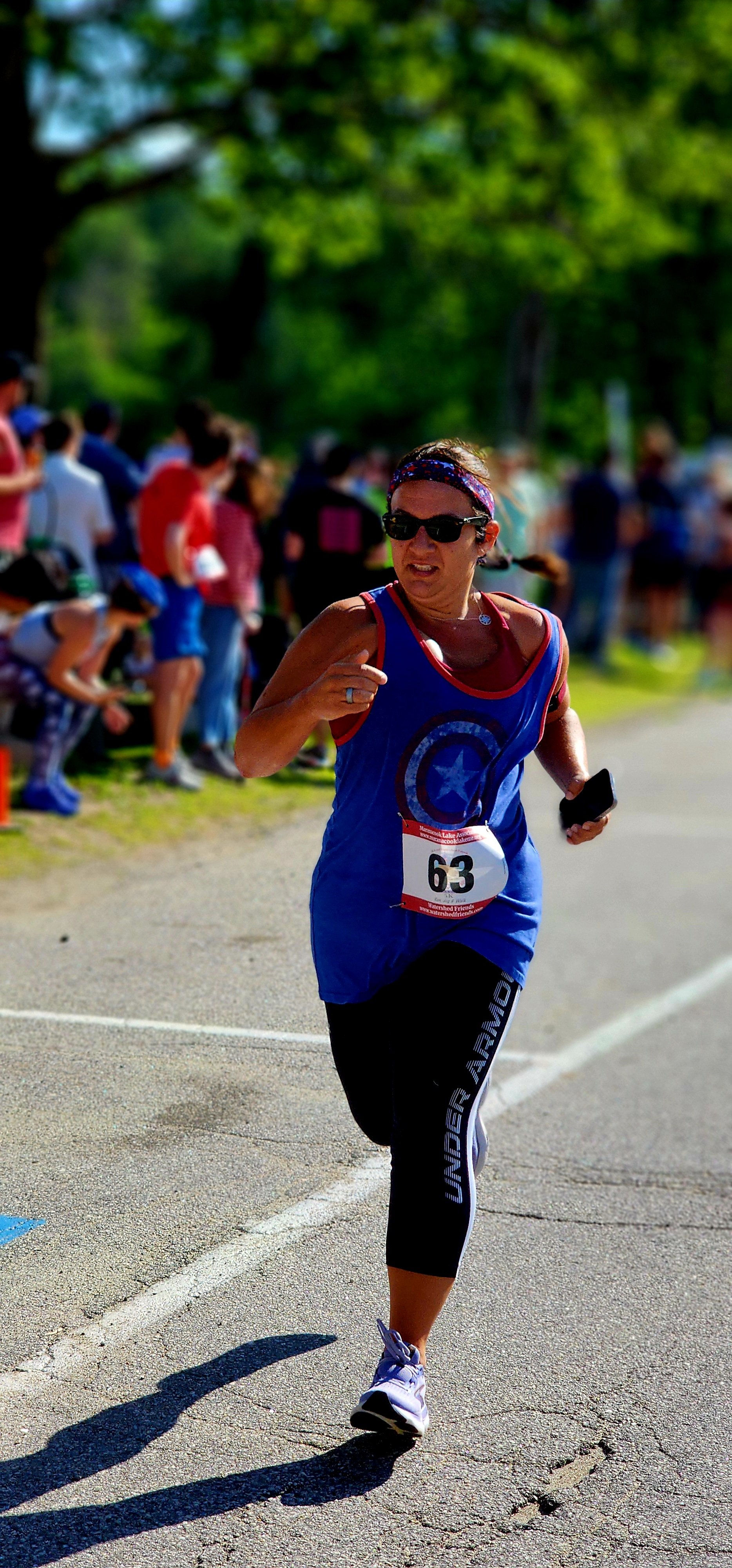 A woman wearing a blue tank top and black leggings running with a crowd standing in the background
