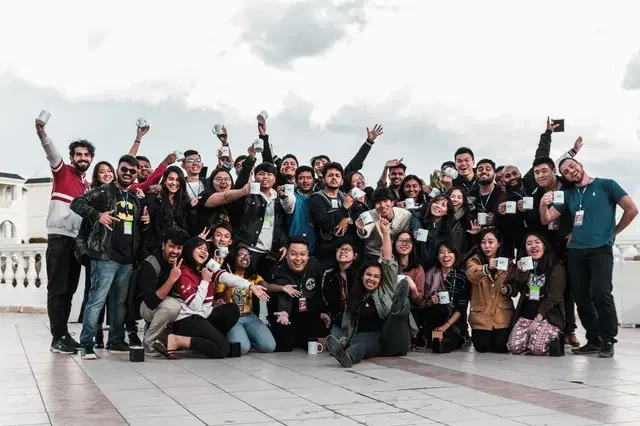 Grupo diverso de personas celebrando con tazas en un espacio abierto bajo un cielo nublado.