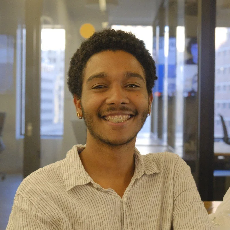 Joven sonriendo en oficina moderna con ventanas grandes y vista a edificios.