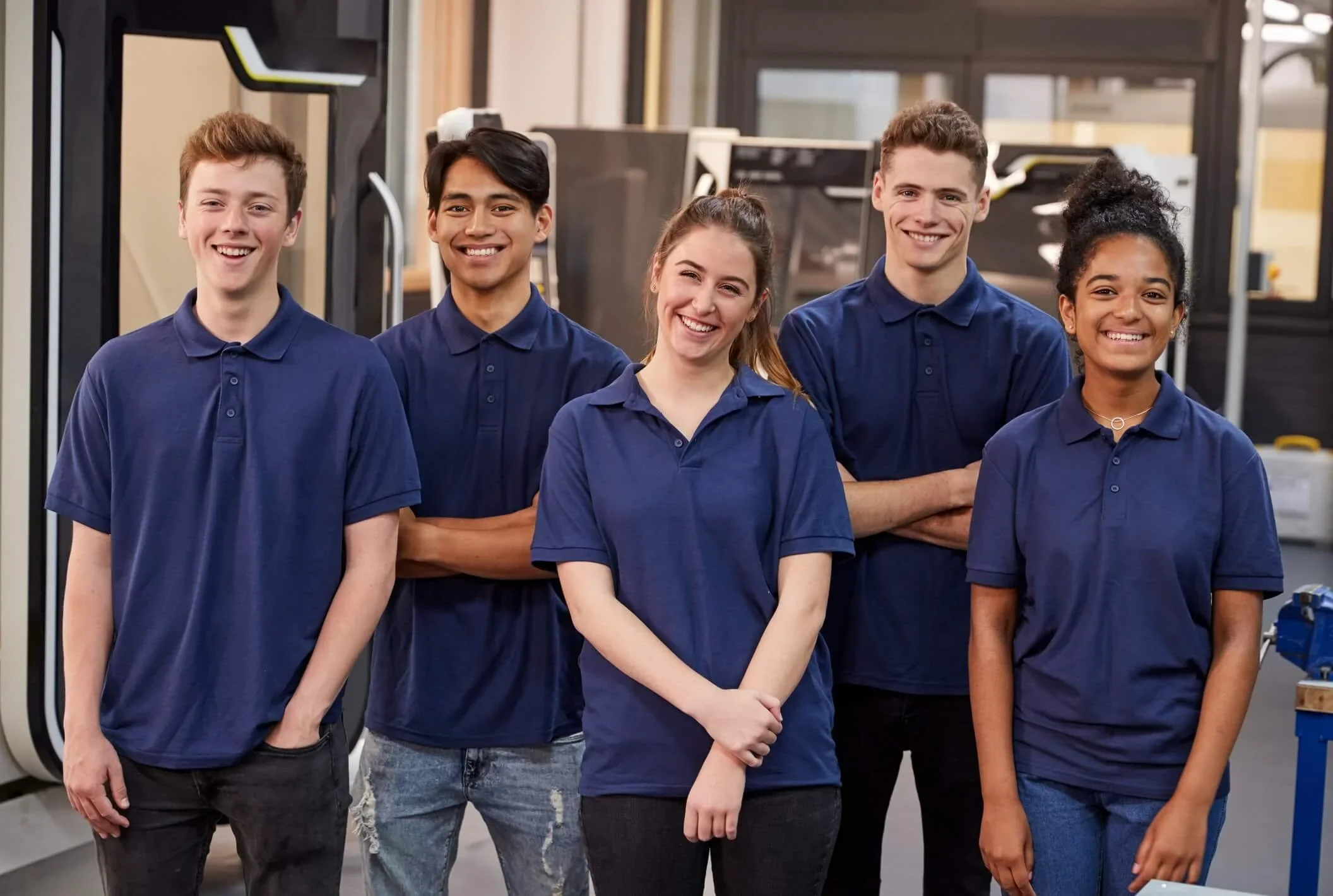 Cinco personas jóvenes en uniforme azul de trabajo en un entorno industrial, sonriendo y posando para la foto.