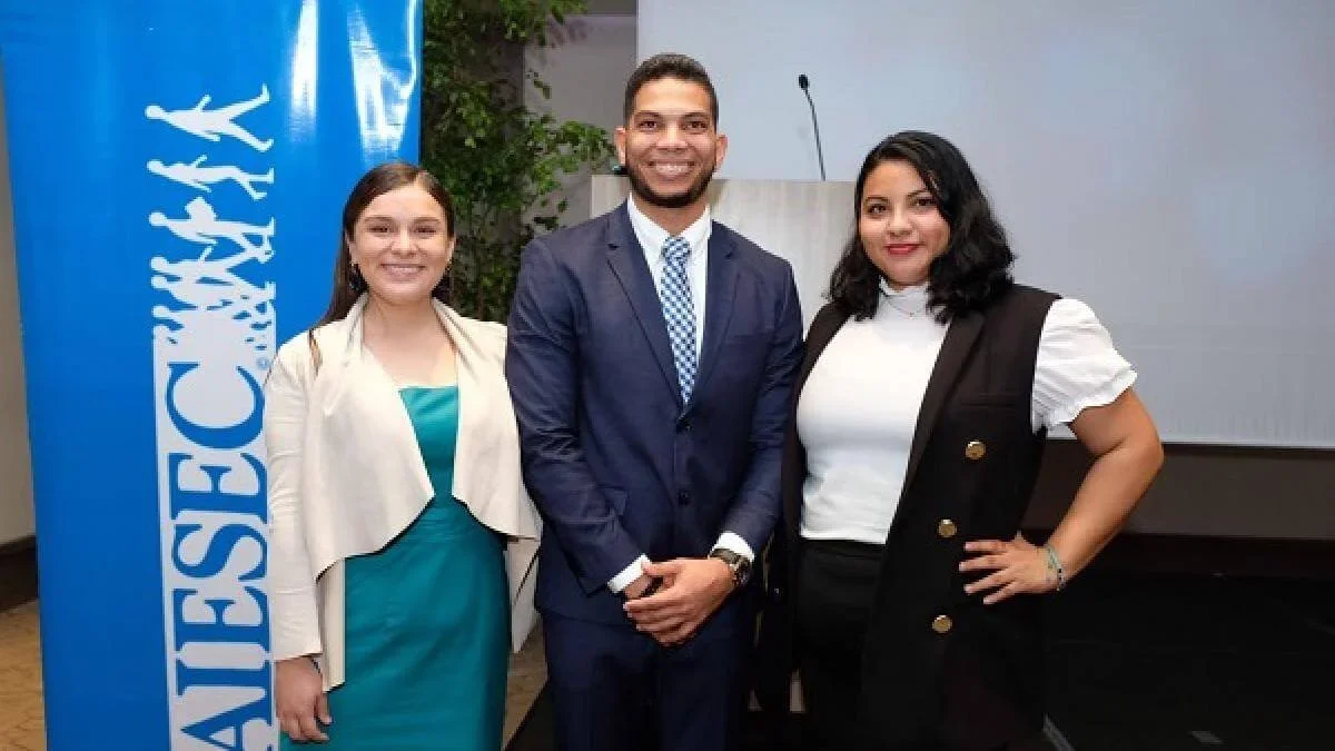 Tres personas posando en un evento con un cartel azul que dice "CIESCAY".
