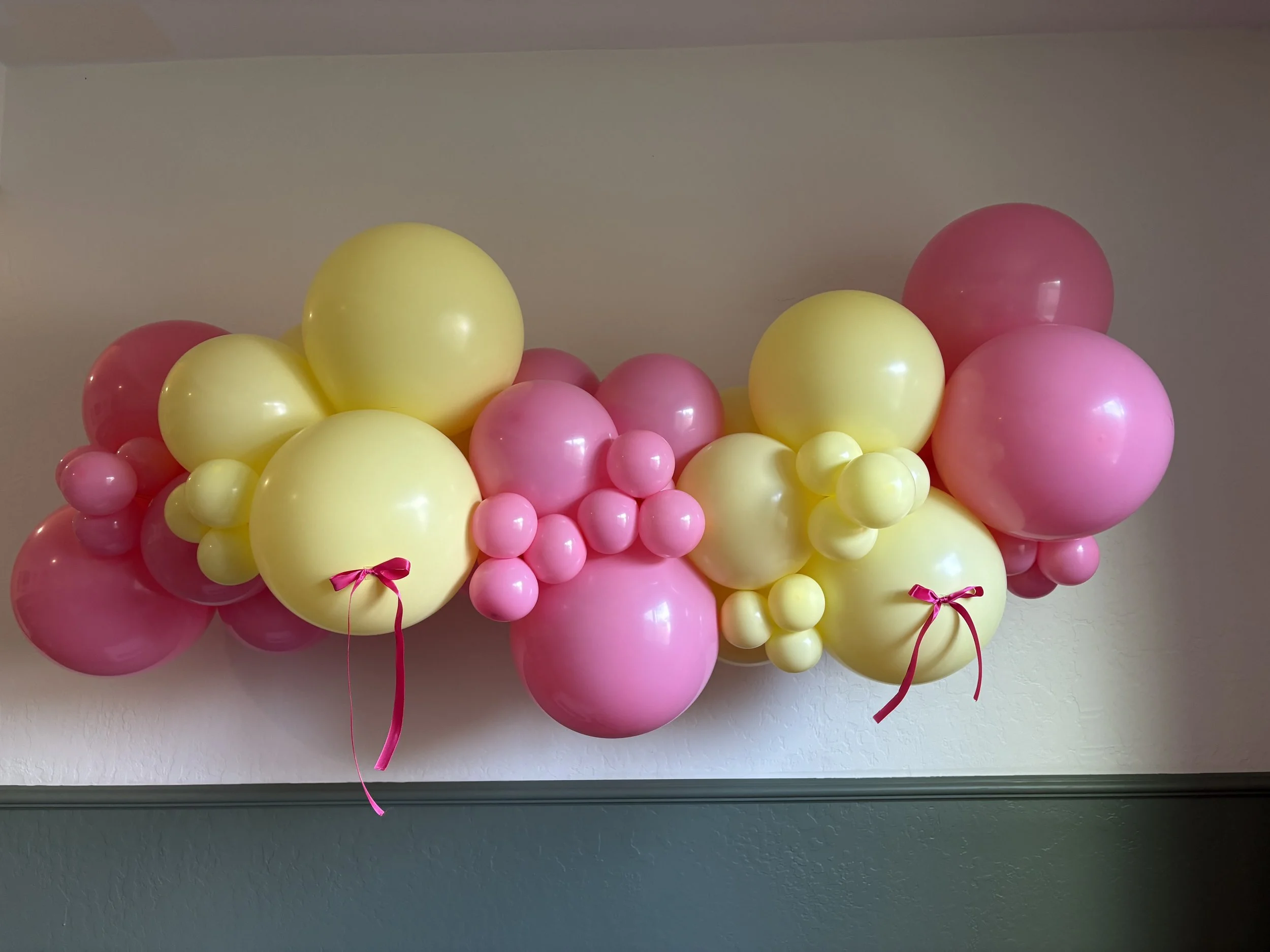 Arrangement of pink and yellow balloons in various sizes, decorated with pink ribbons.