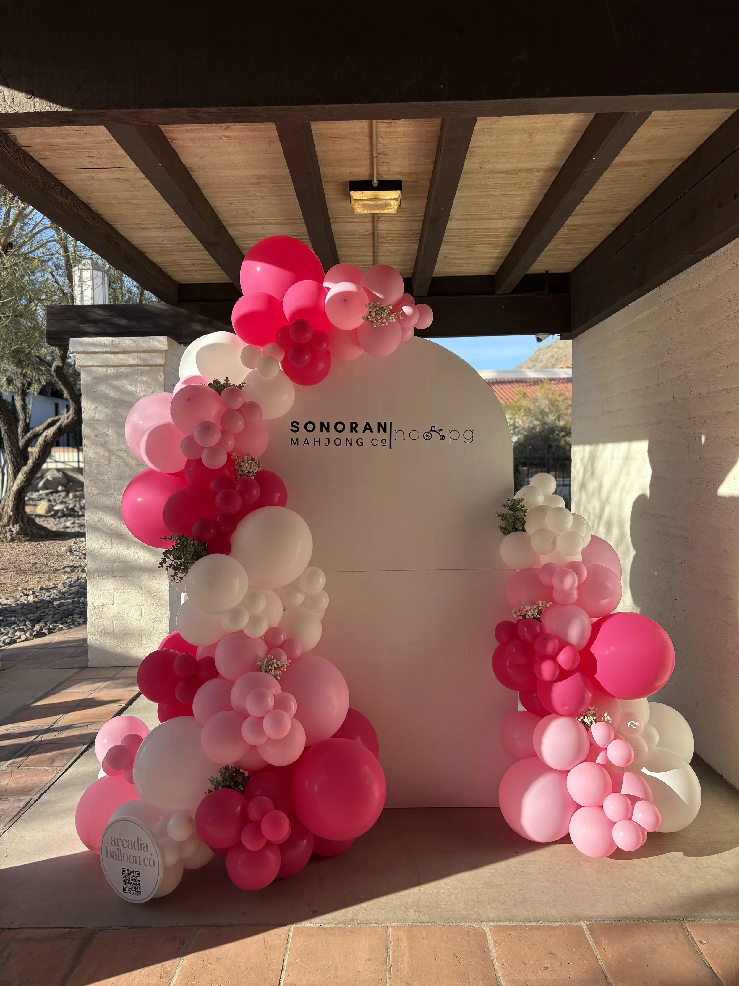 Decorative balloon arch in shades of pink and white surrounding a white circular backdrop at an outdoor event.