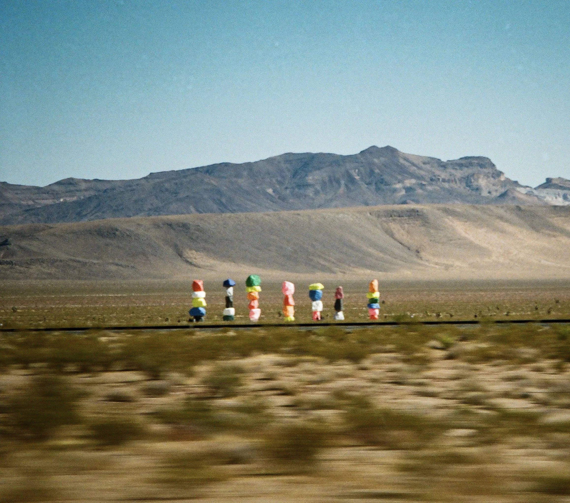 A desert landscape with a mountain range in the background, and colorful stackable objects in the foreground.