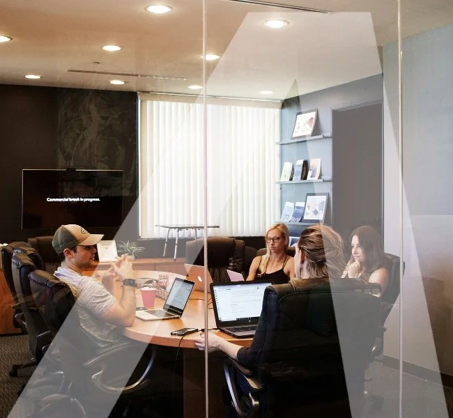 Business meeting in a conference room with four people working on laptops, seen through a glass wall.
