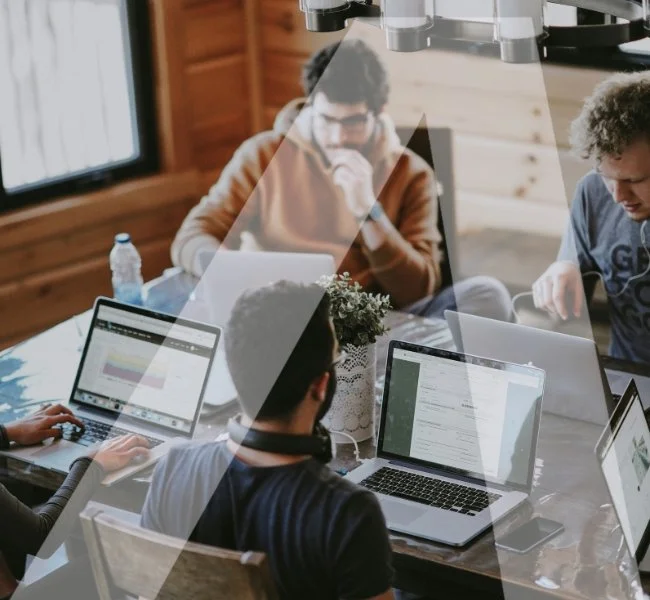 Group of four people working on laptops around a table in a wooden-paneled room.