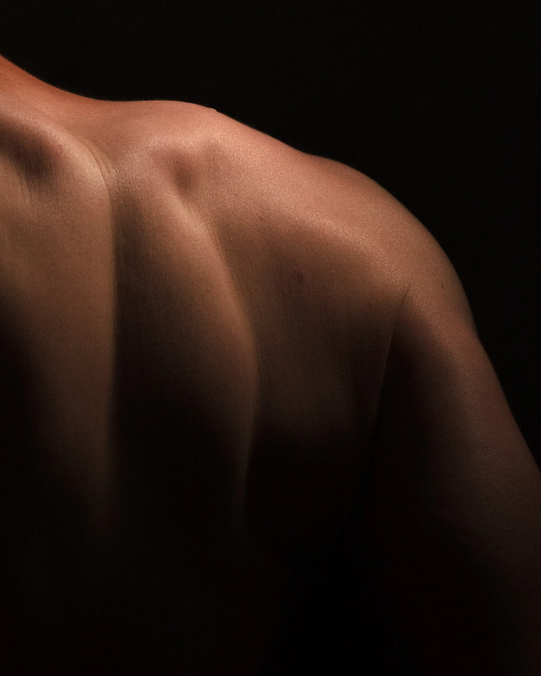 Close-up of a person's shoulder and upper arm, draped in sheer, skin-tone fabric against a dark background.