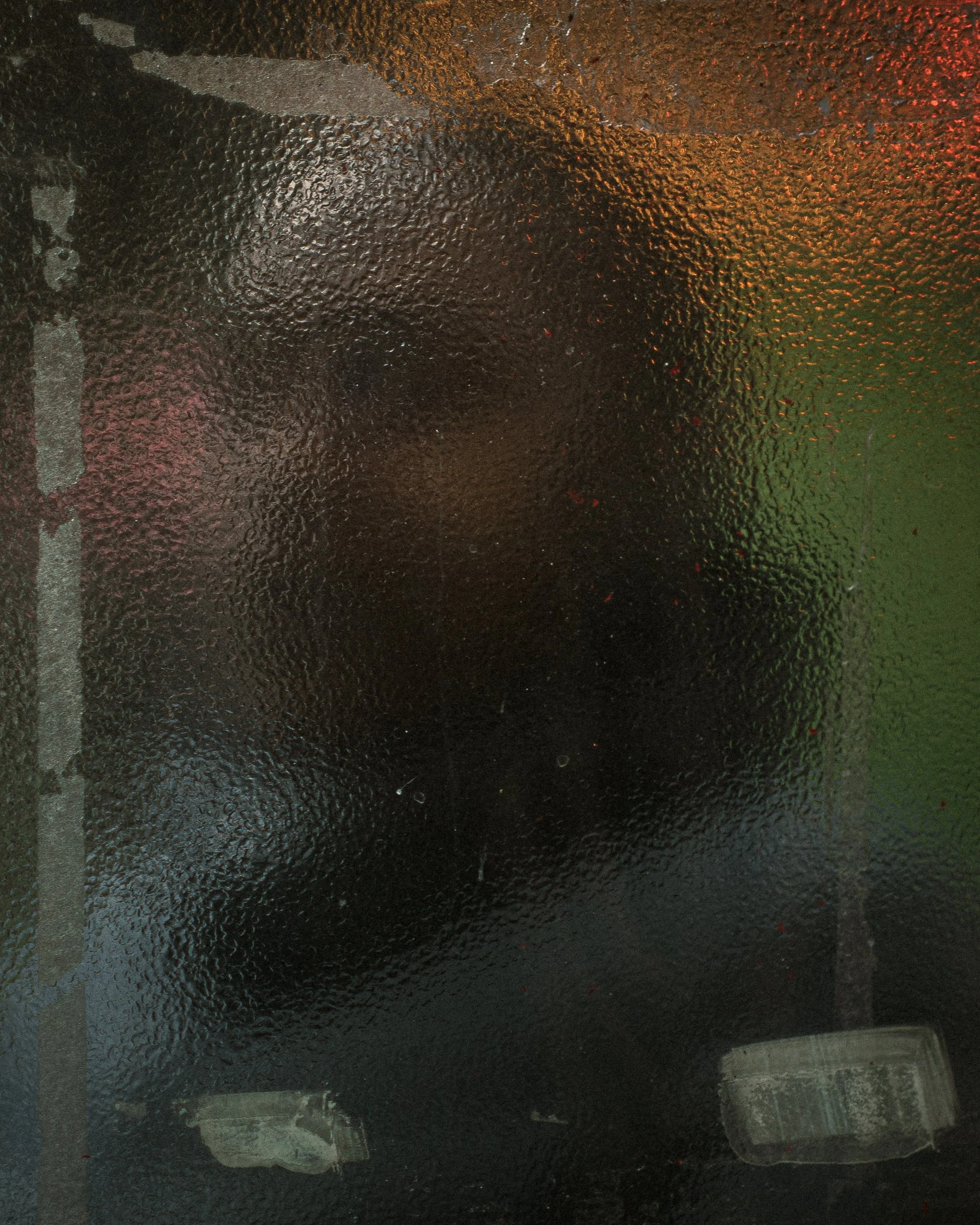 Person standing behind a textured, frosted glass surface with light reflections.