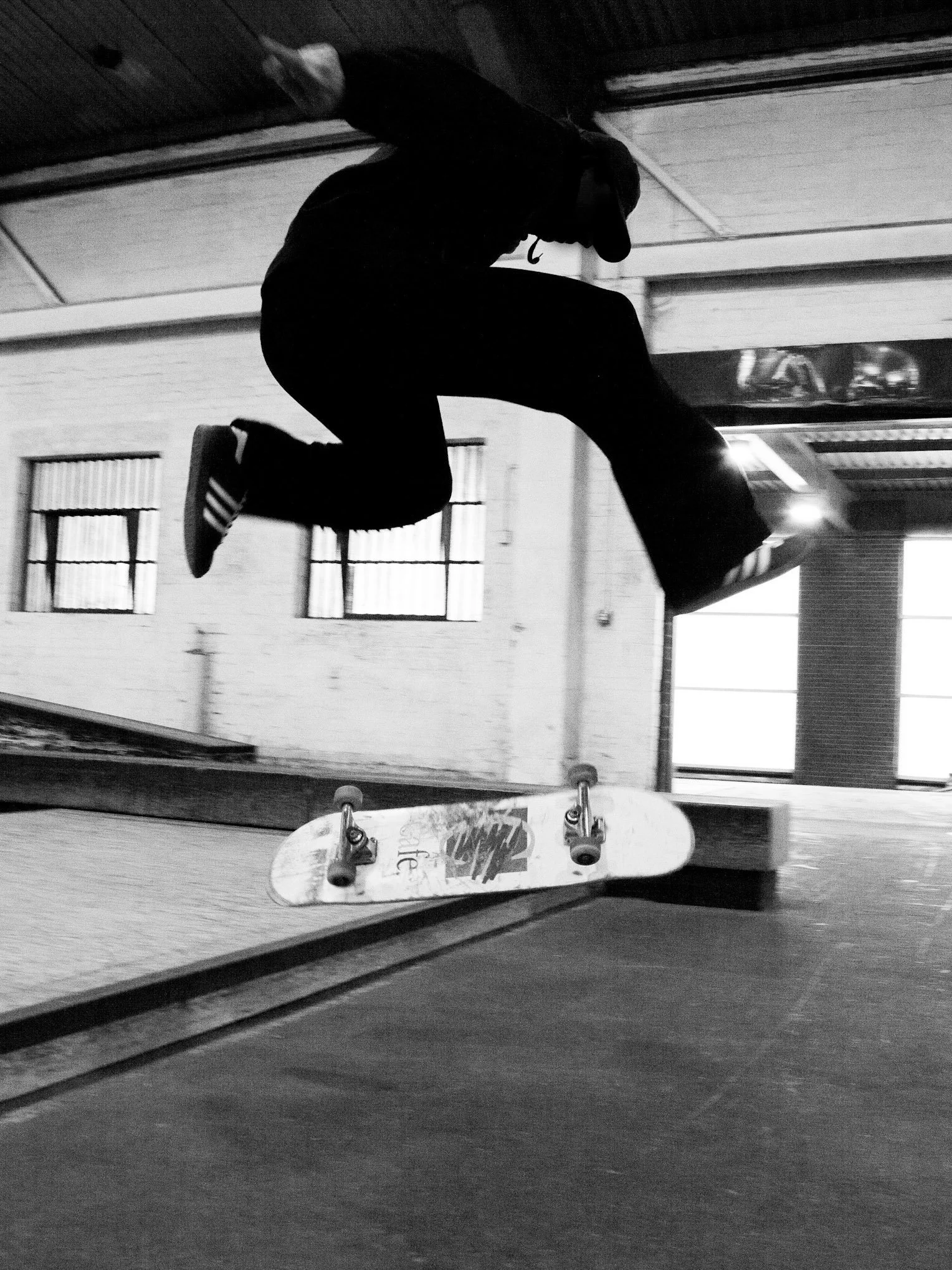 Skateboarder performing a jump at an indoor skatepark in black and white.