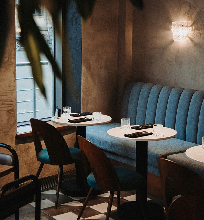 Upscale restaurant interior with blue banquette seating, round tables, and warm ambient lighting.