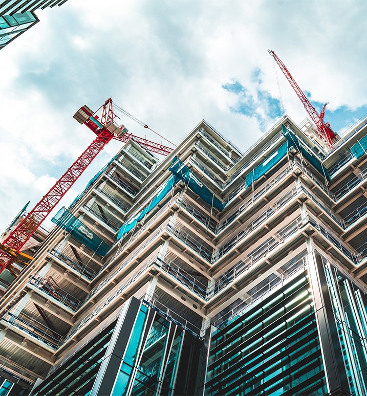 Modern high-rise building under construction, viewed from below with multiple construction cranes against the sky.
