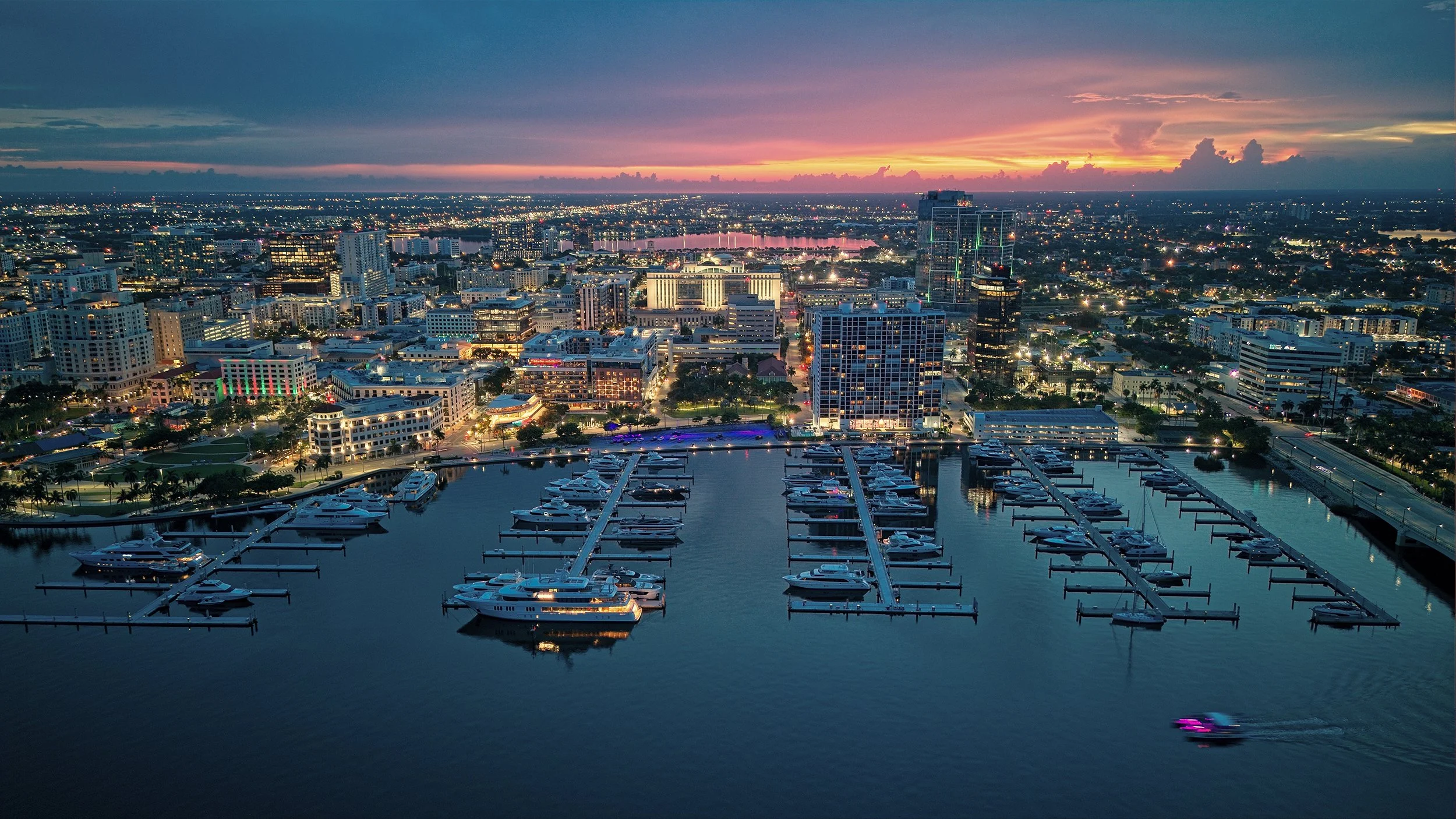 Aerial view of a marina and waterfront city skyline at sunset.
