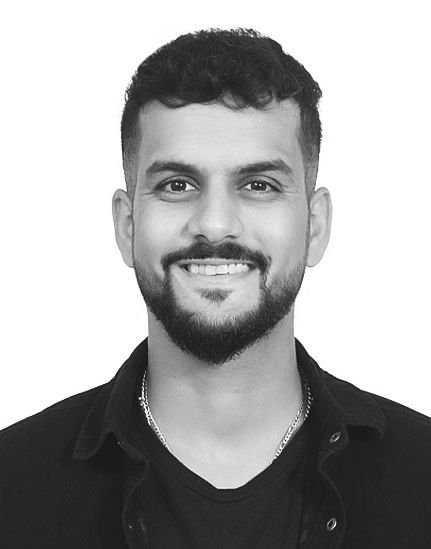 Black and white portrait of a man with short curly hair, a beard, and a mustache, smiling at the camera.