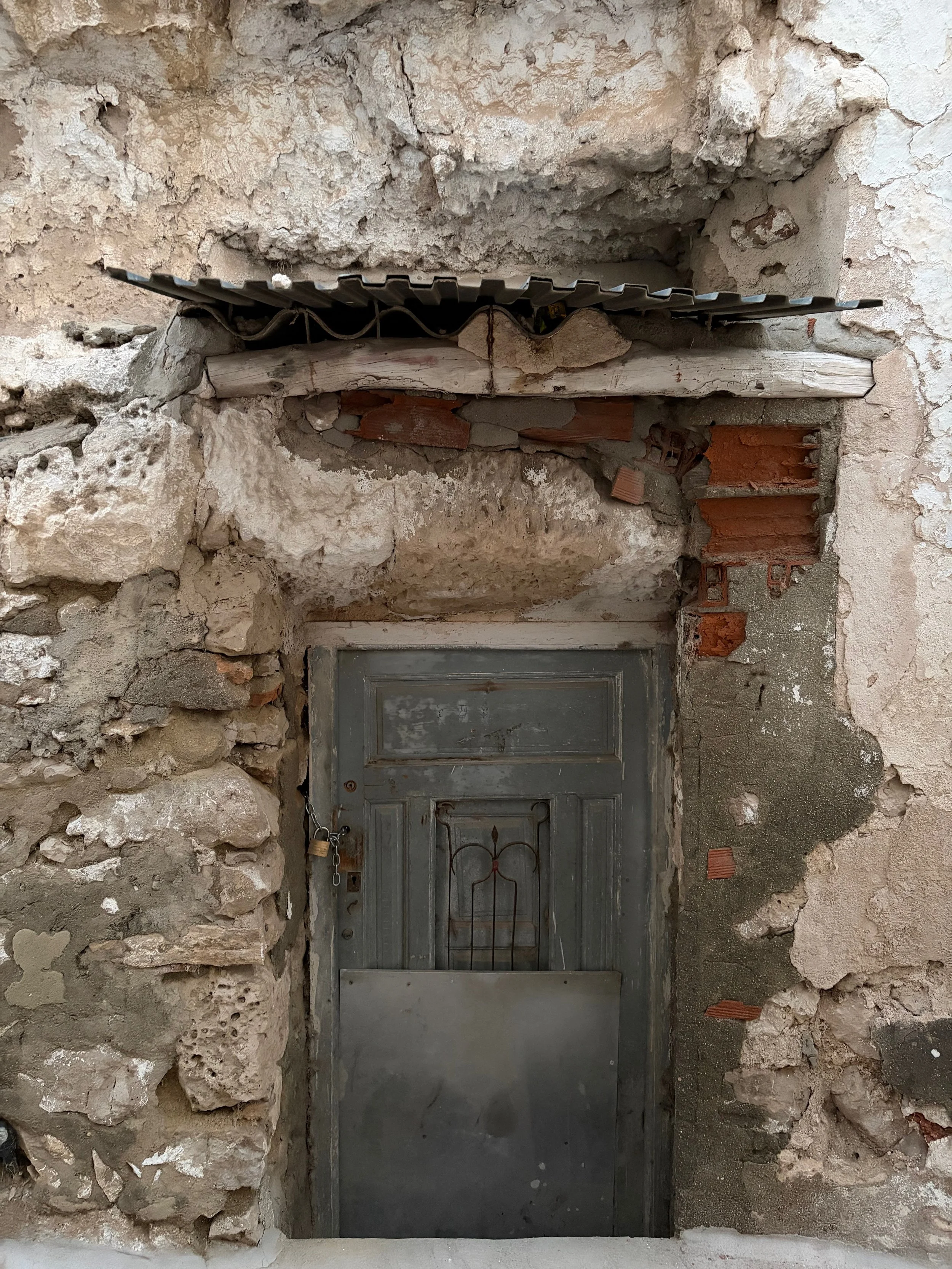 Old weathered door of a dwelling built within a cave in a traditional Spanish village. The entrance is surrounded by stone and brick. Doors are a metaphorical for curiosity, being open, and being grounded