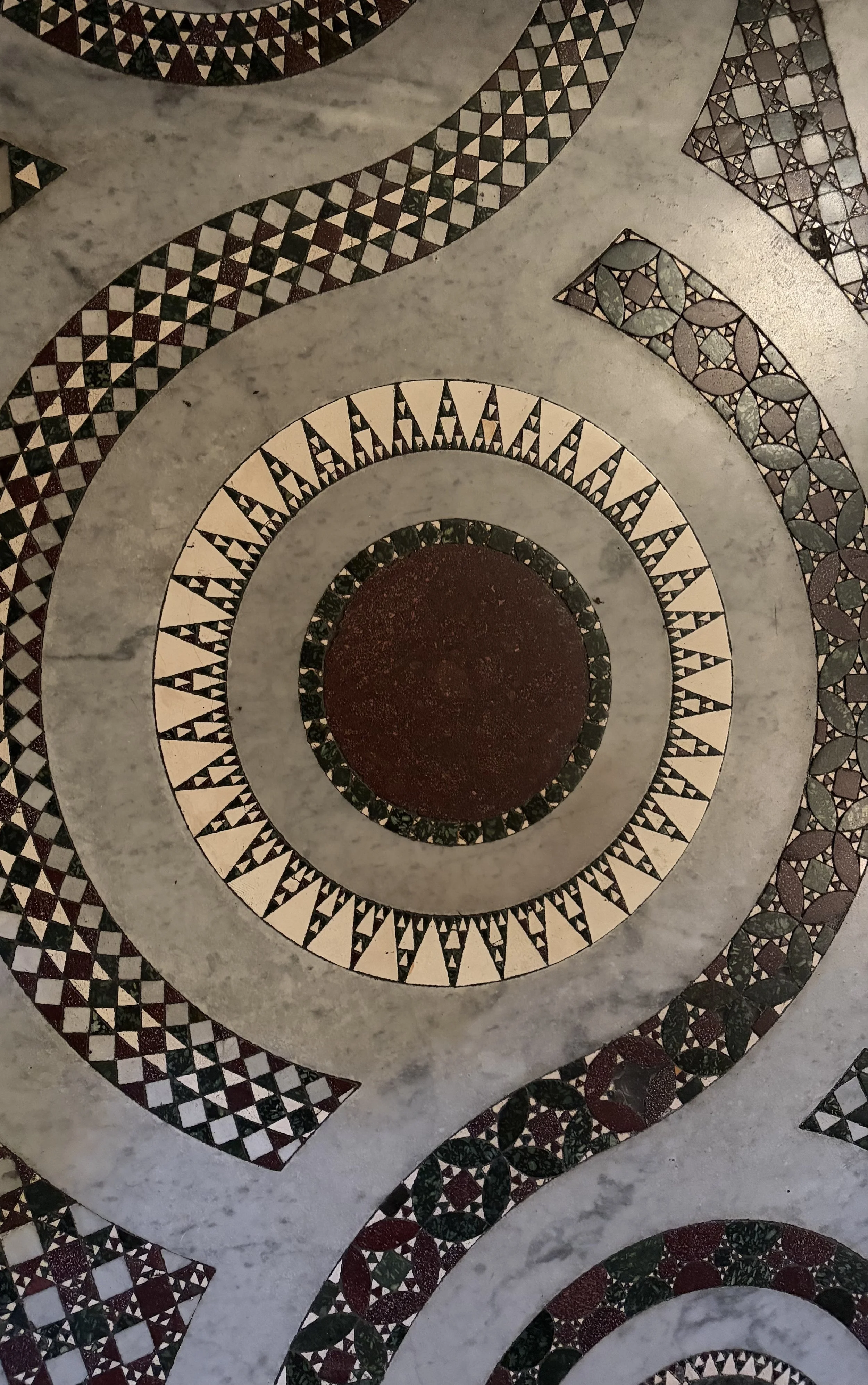 Close-up view of an intricate mosaic pattern featuring concentric circles with geometric designs in black, white, green, and red on a marble surface.