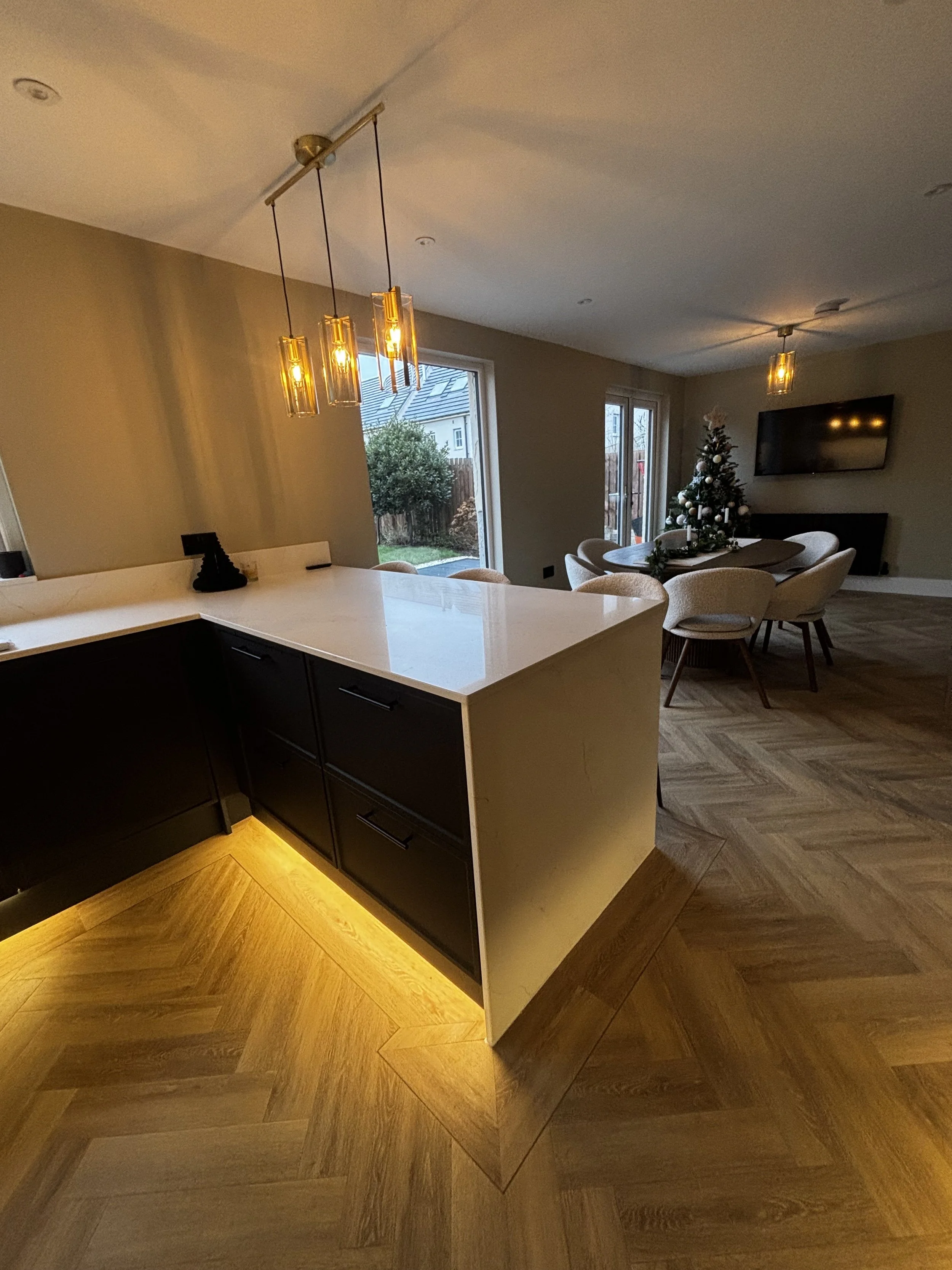 Open-concept living and kitchen area with hardwood floors, modern hanging pendant lights, a marble-topped kitchen island, and a decorated Christmas tree in the dining area.