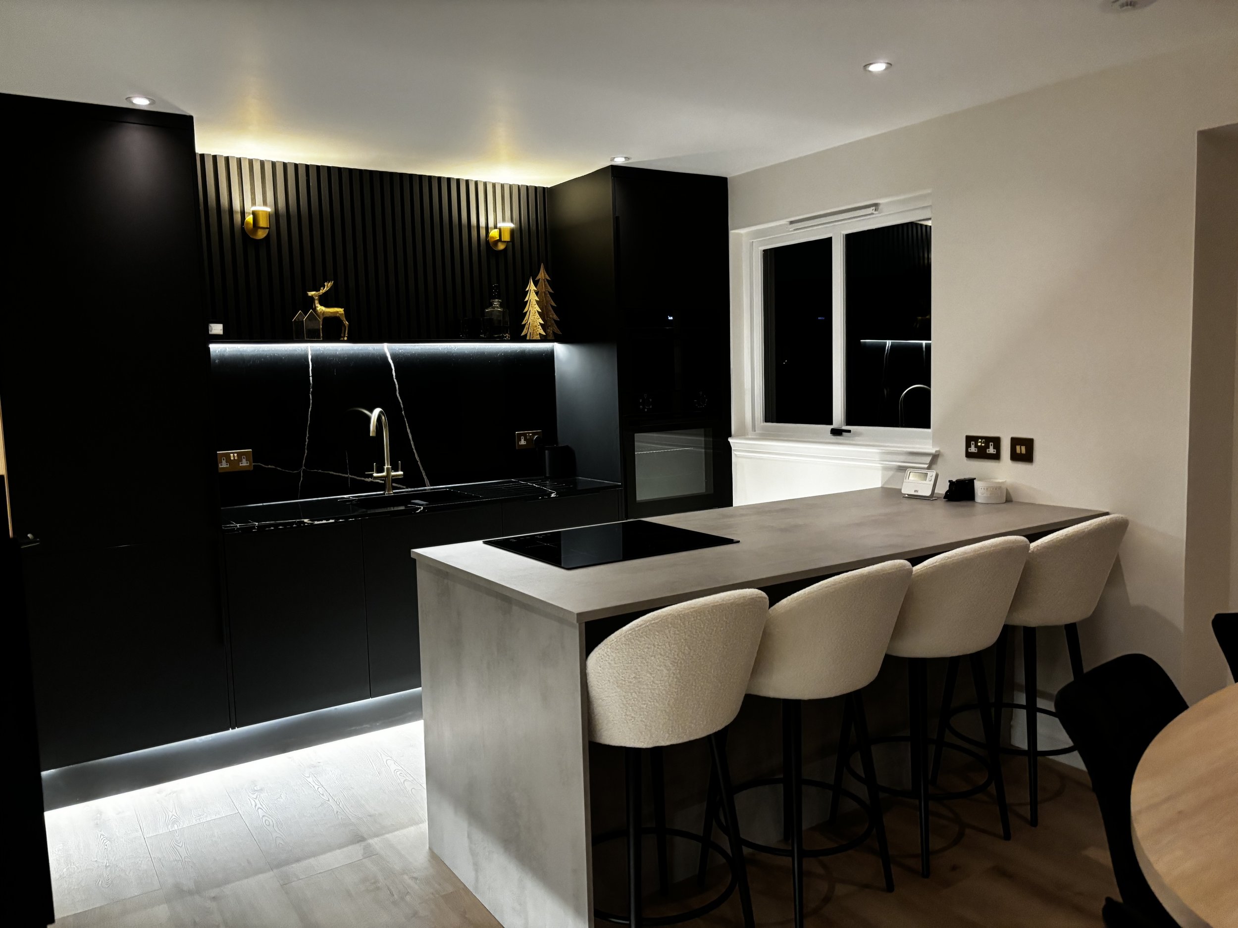 Modern kitchen with black cabinetry, marble backsplash, beige bar stools, and a light-colored countertop.