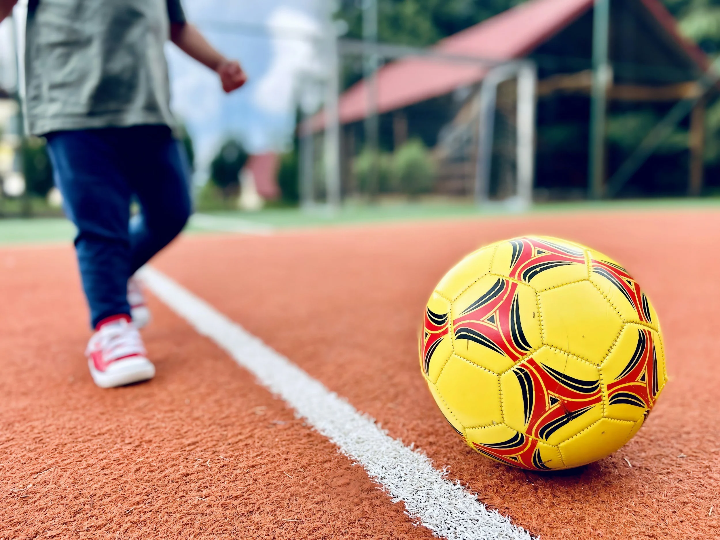 Enfant en vêtements décontractés et baskets jouant au football sur un terrain en plein air.